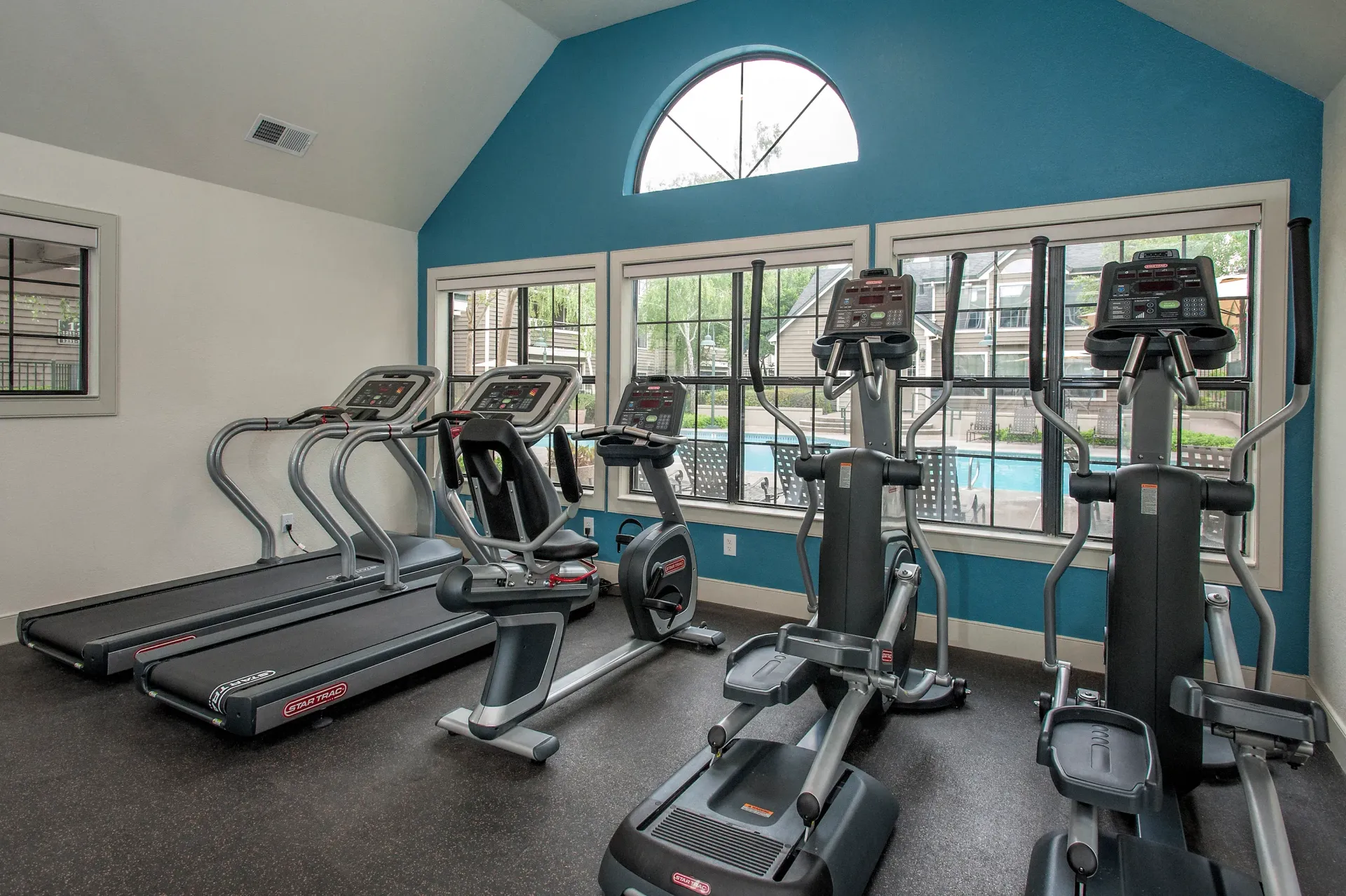 Cardio fitness room with treadmills, ellipticals, and bikes by a large window and blue wall at The Reserve at Capital Center.