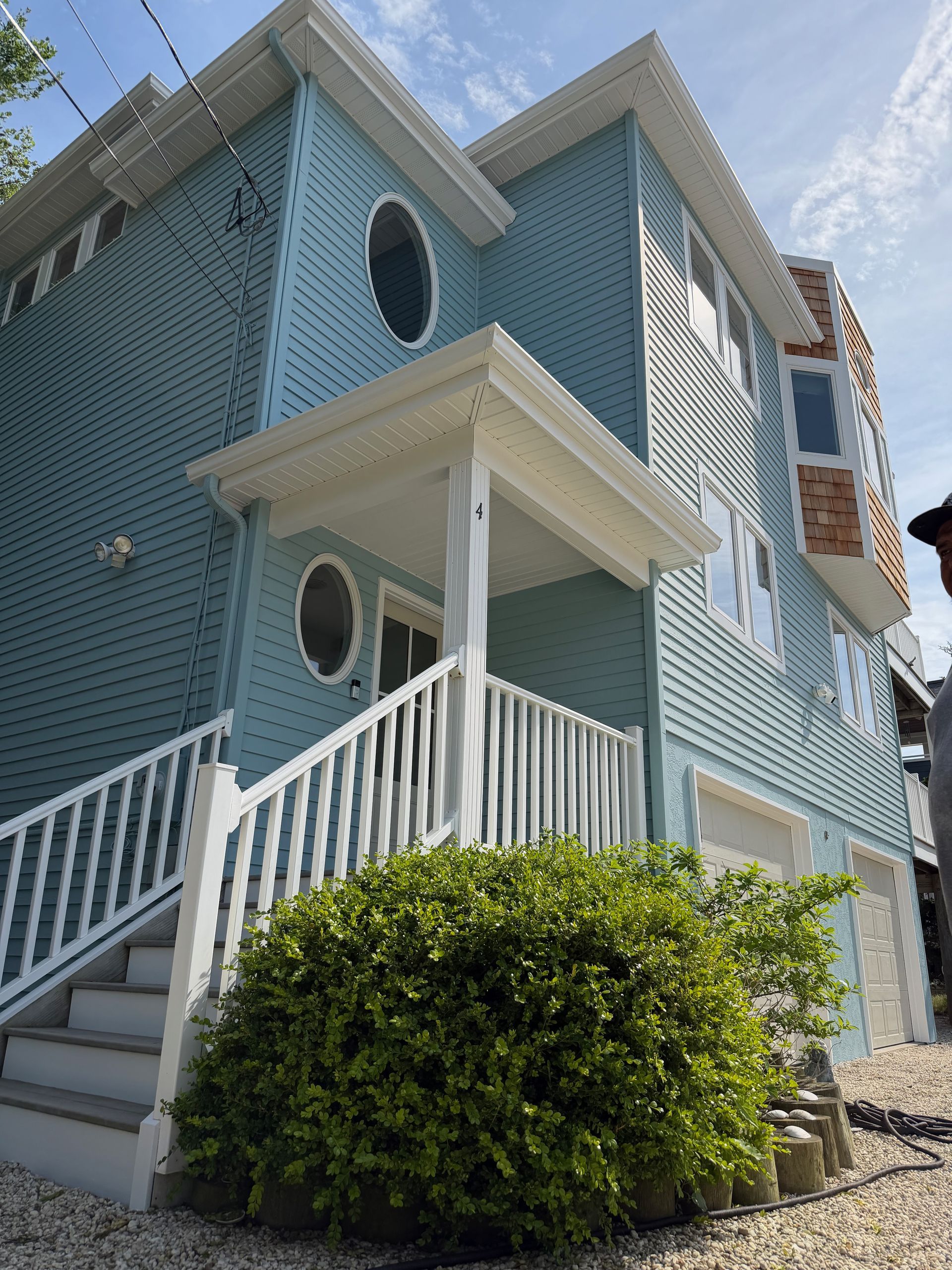 Blue coastal house with white trim, porch stairs, and round windows beside a green shrub