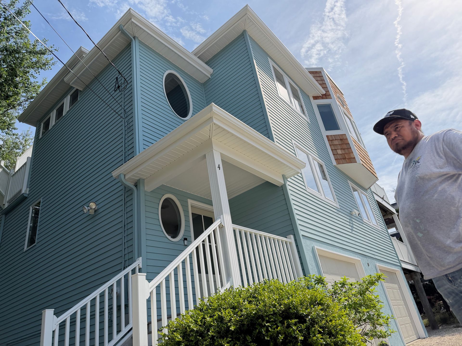 Blue two-story house with white trim and porch, viewed from below, with a man standing at the right edge.