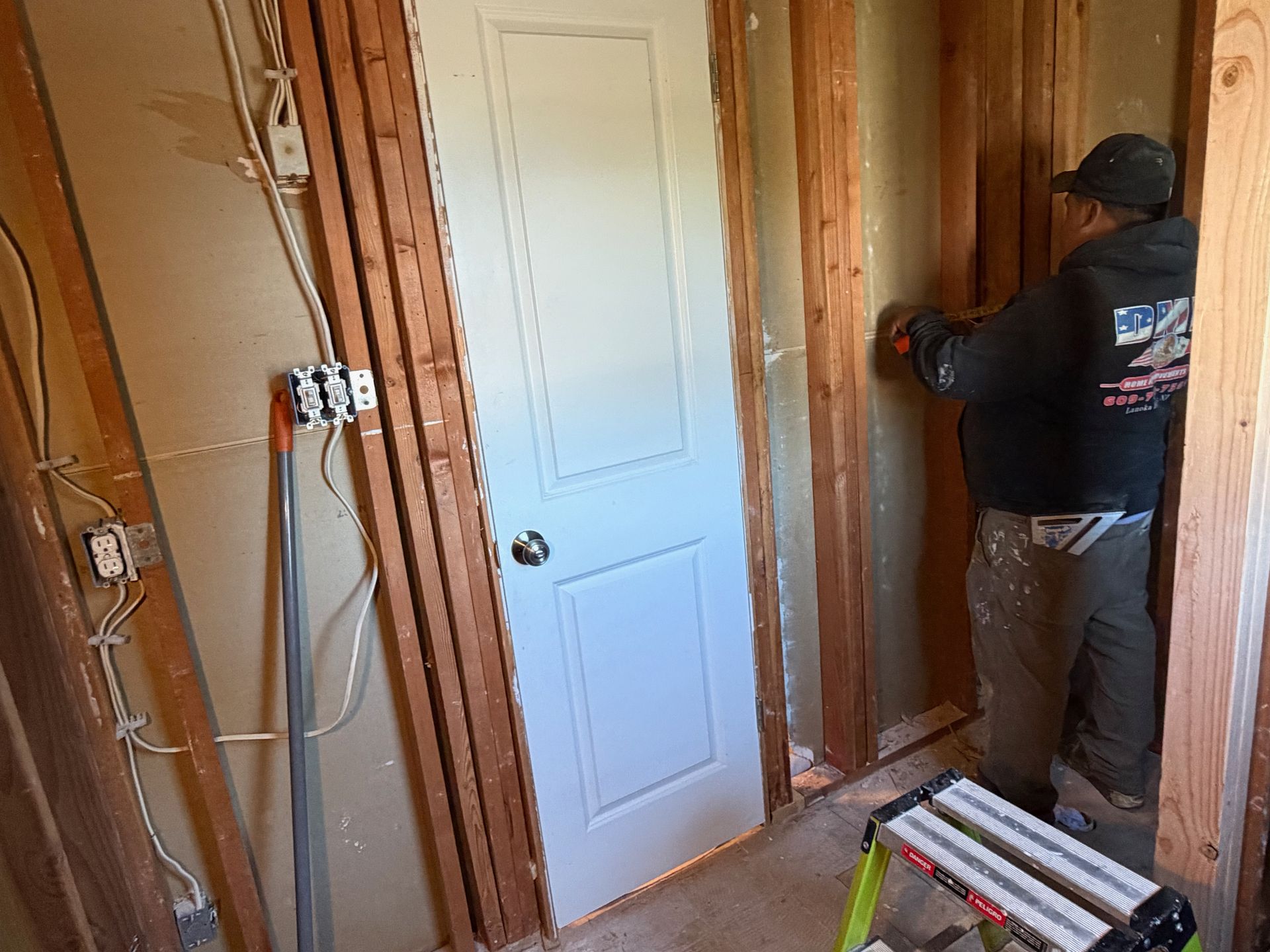 Person installing wiring in an unfinished room beside a white door and exposed studs