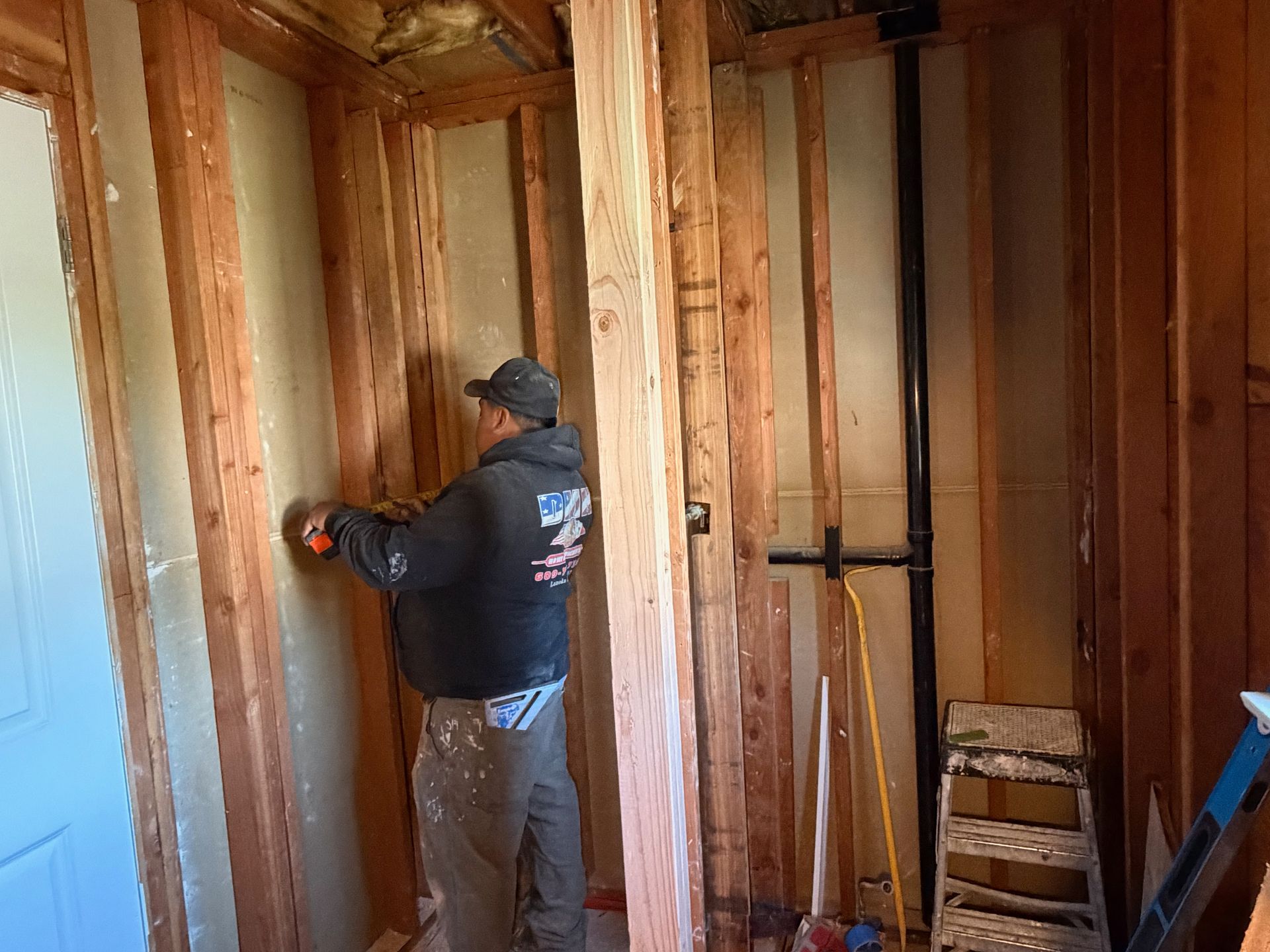 Worker measuring wall studs inside a framed room under construction
