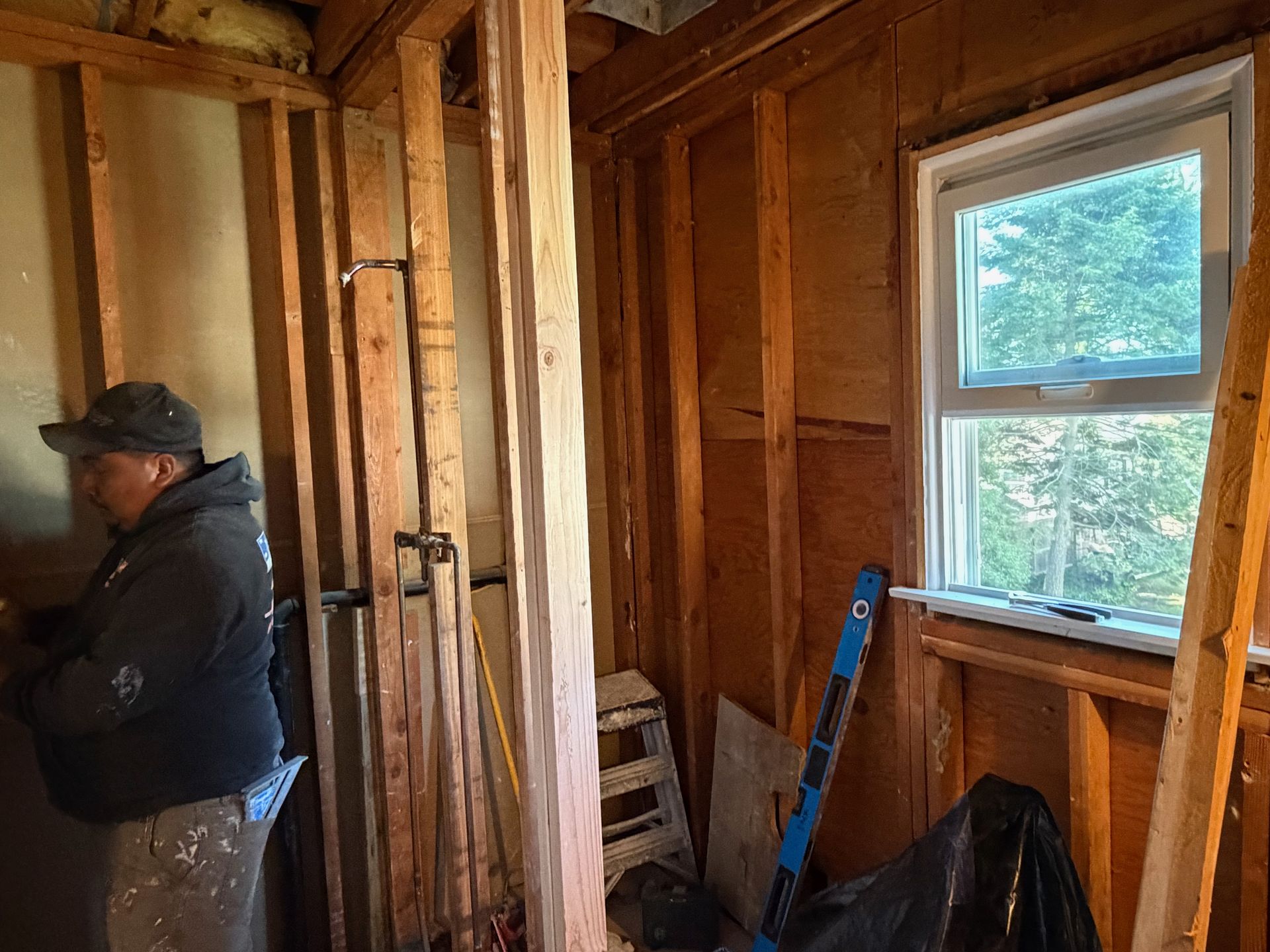Worker in a partially finished wooden room holding tools near a window.