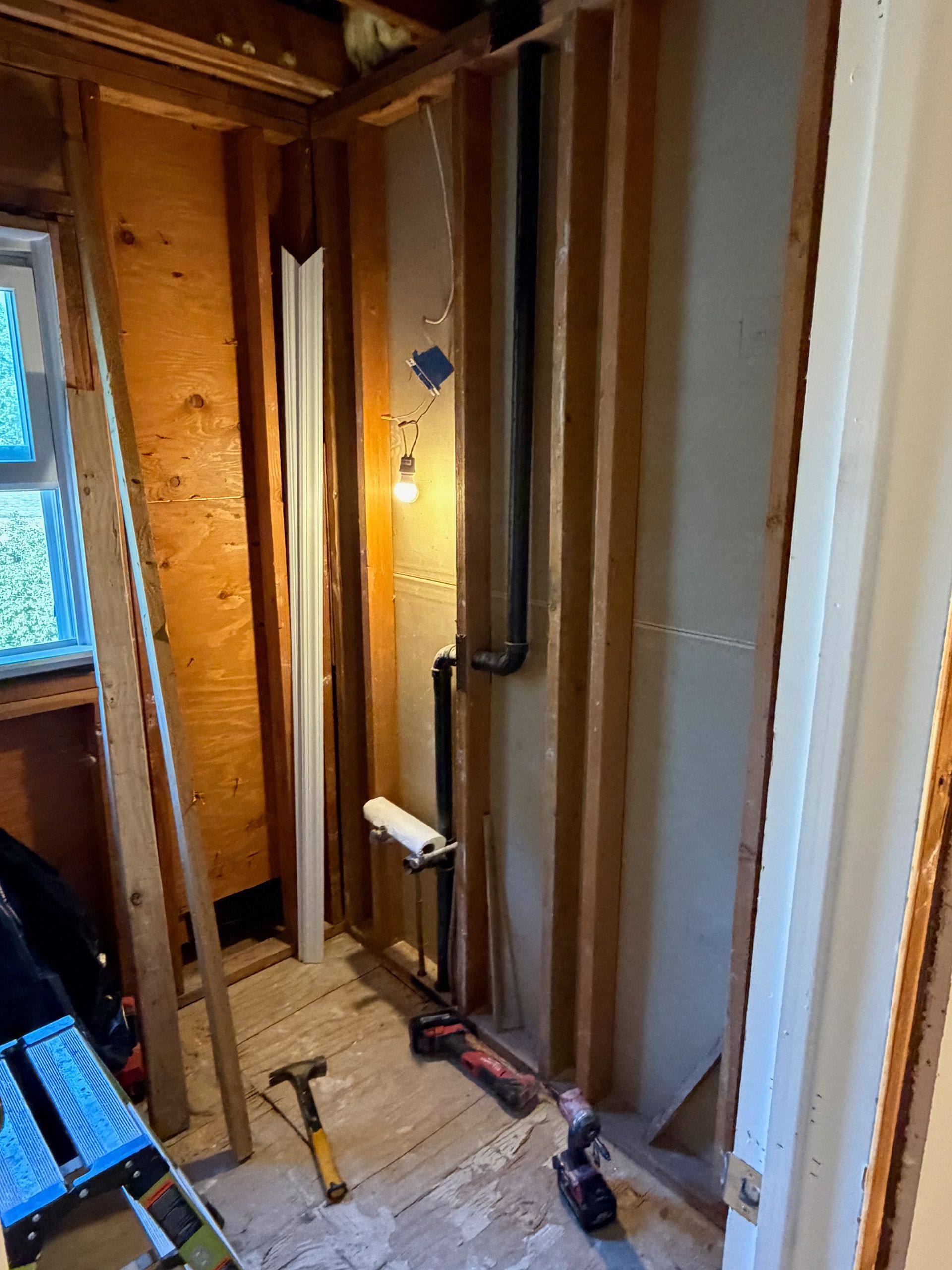 Exposed wall framing and plumbing in a narrow unfinished room under construction