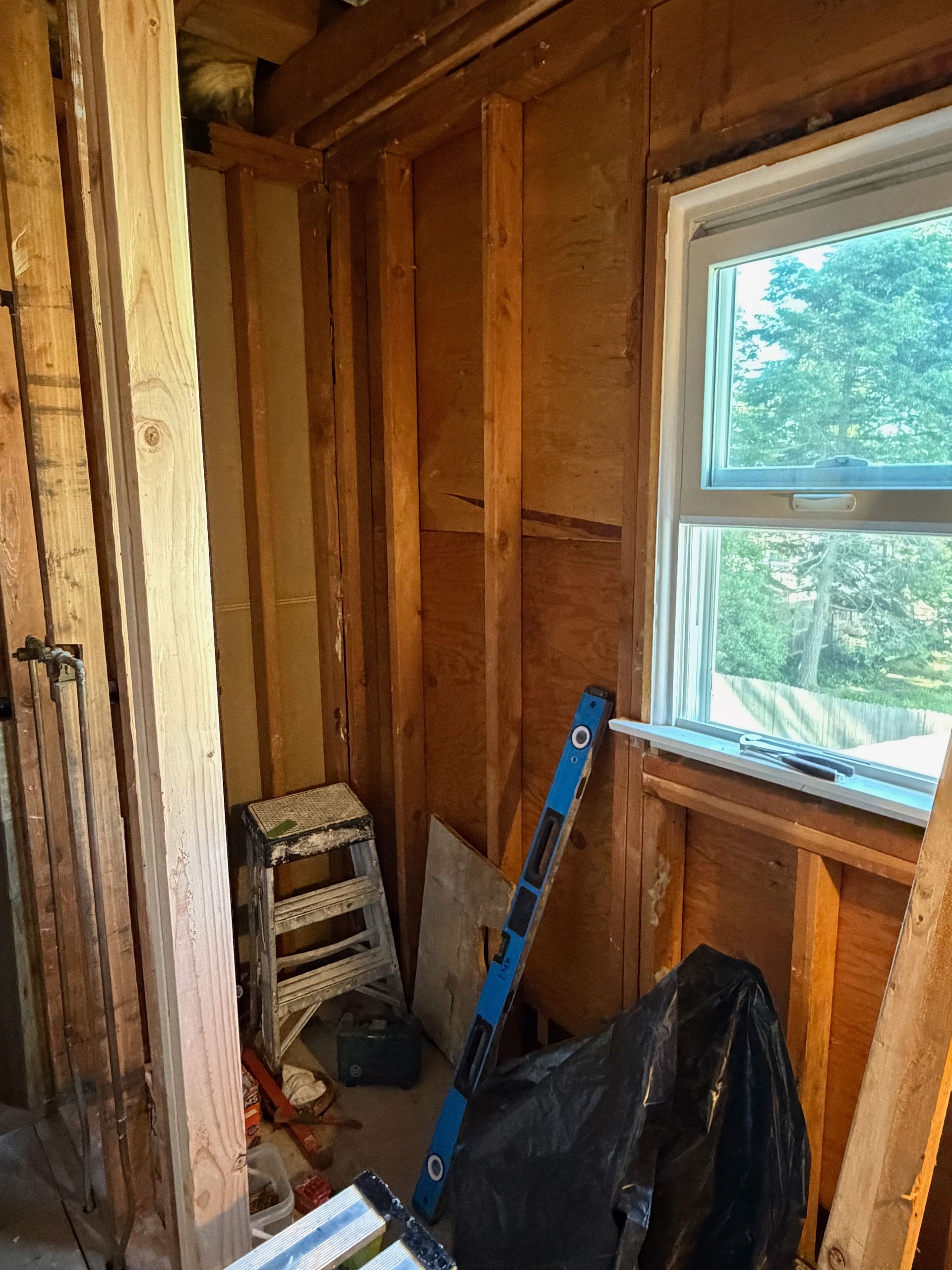 Partially renovated room with exposed studs, a window, and tools leaning against the wall