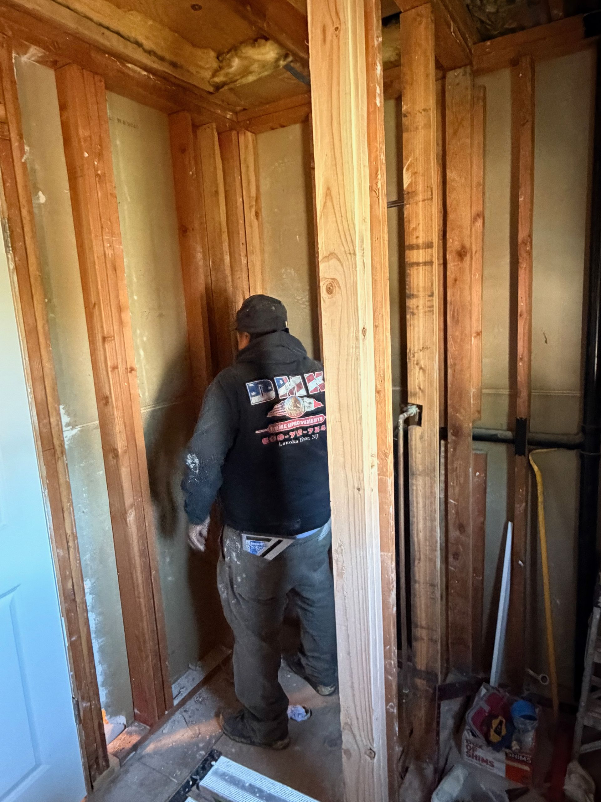 Worker standing in a stripped room framed with exposed wooden studs, preparing interior wall construction