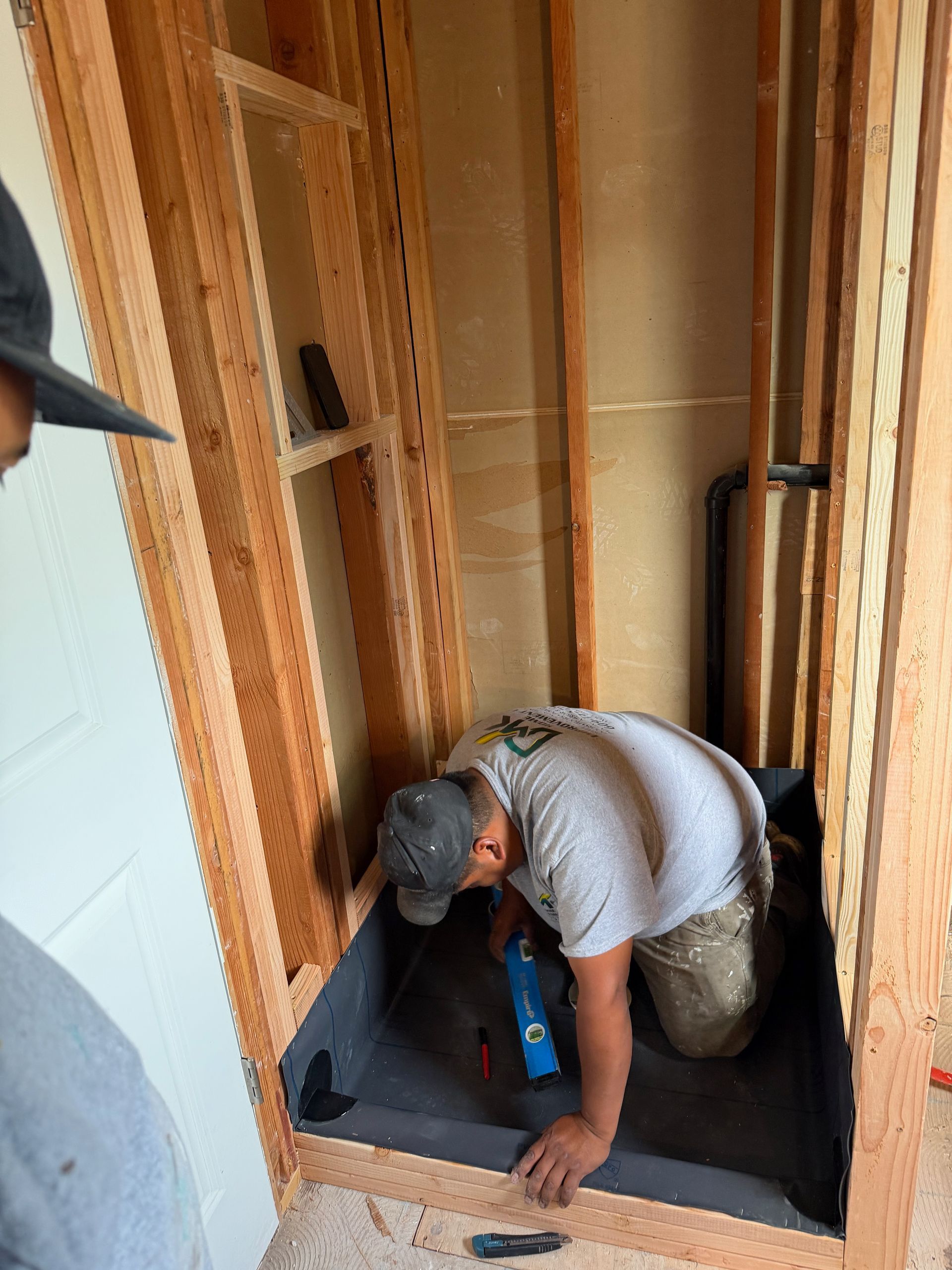 Worker kneeling on a subfloor inside framed walls, installing material during home construction.