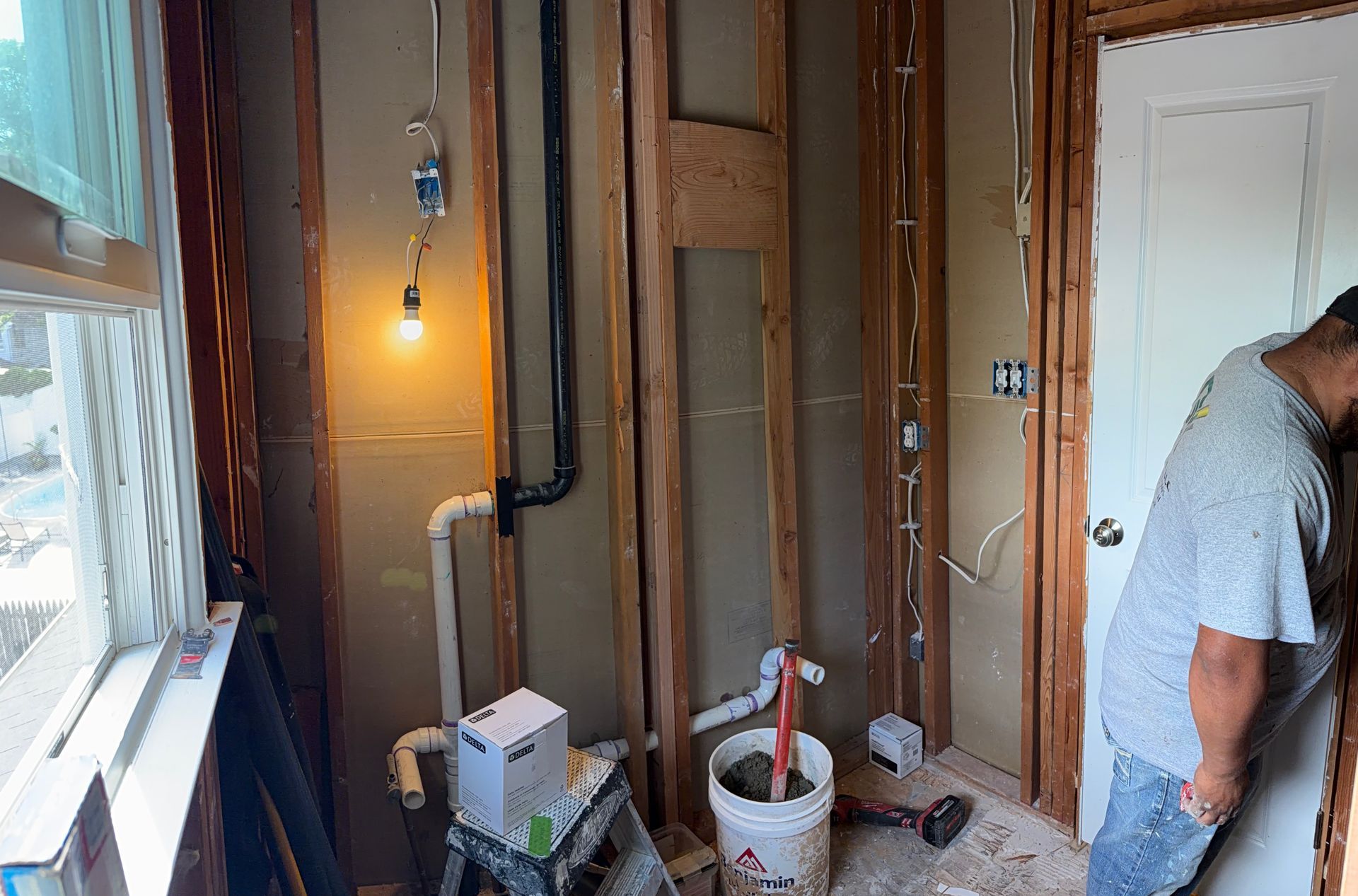 Partially finished room with exposed wall framing, tools, and a worker near the door