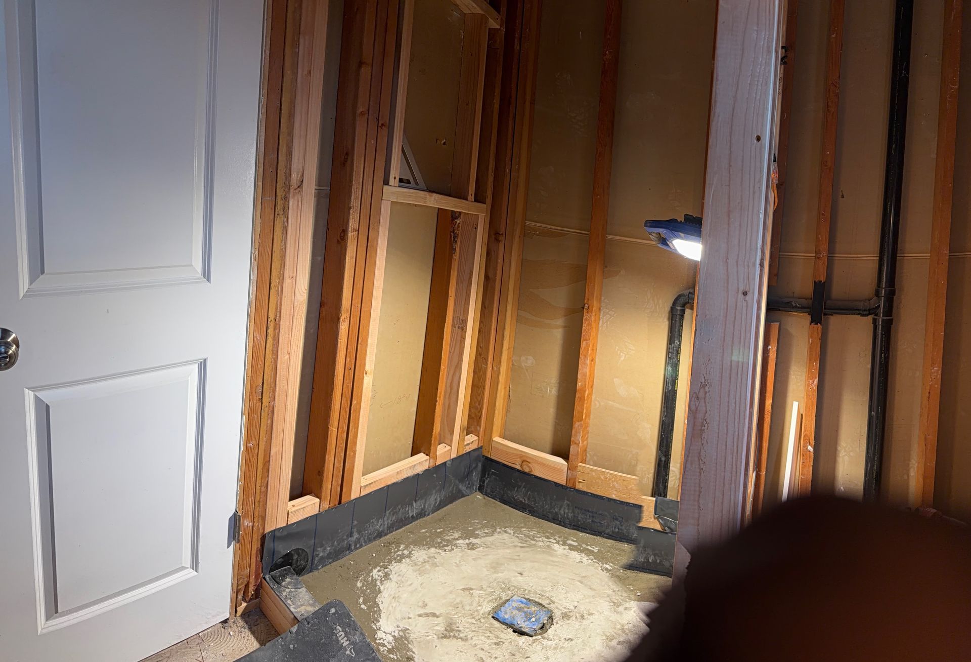 Unfinished bathroom shower area with exposed framing, a white door, and a lit shower niche.
