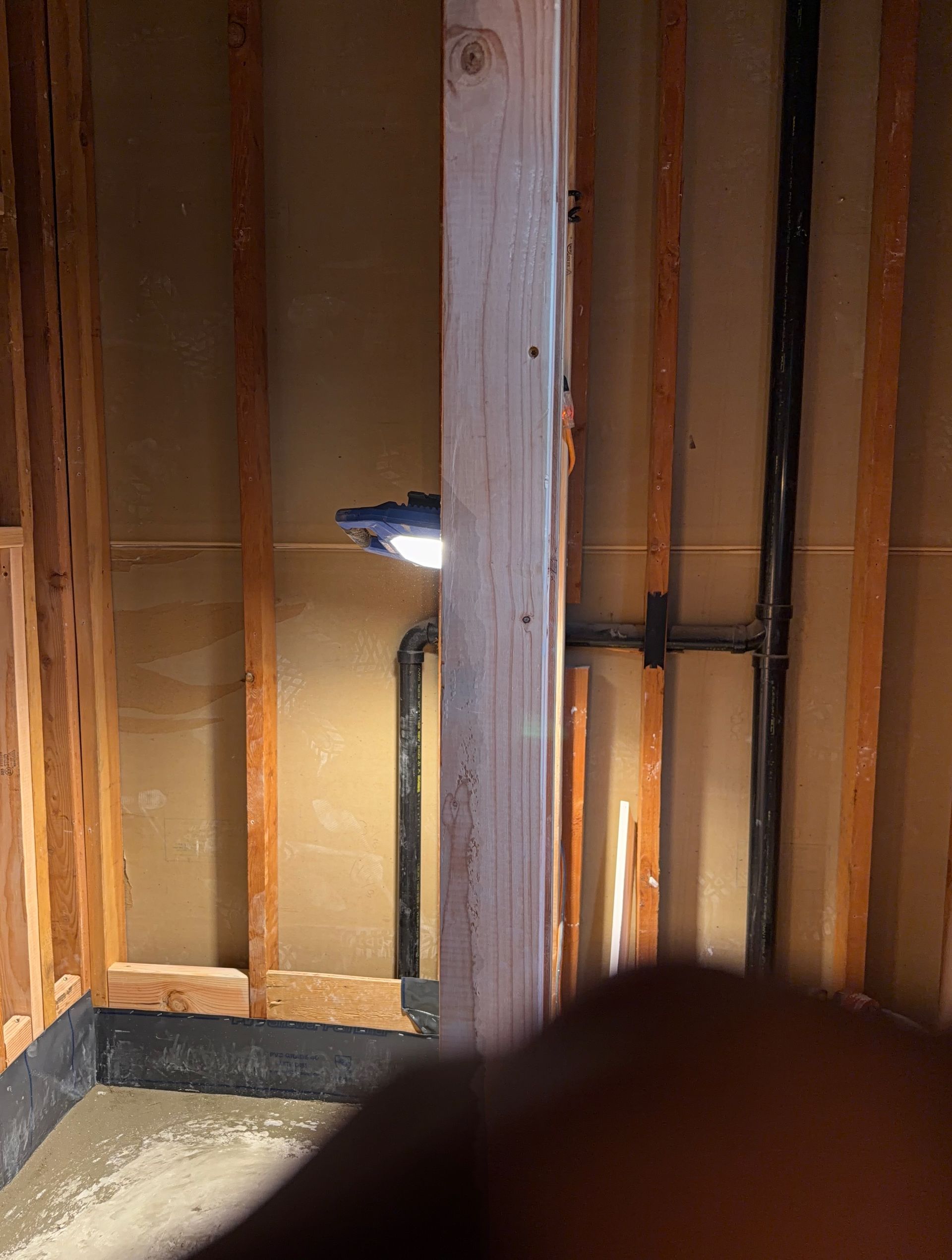Exposed wall framing with insulation, a small wall light, and a blurred finger in the foreground