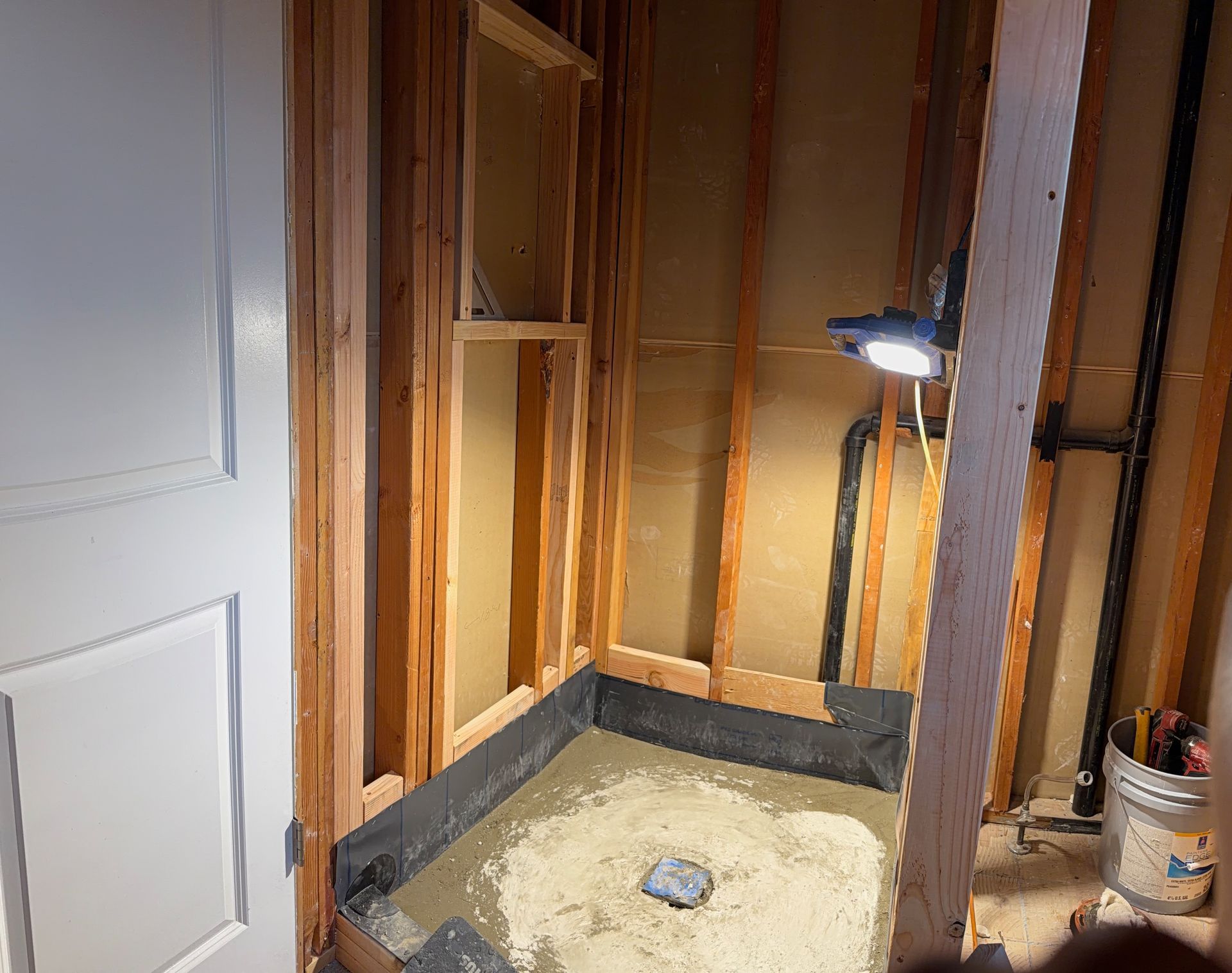 Partially stripped bathroom under renovation with exposed framing, insulation, and a shower base.