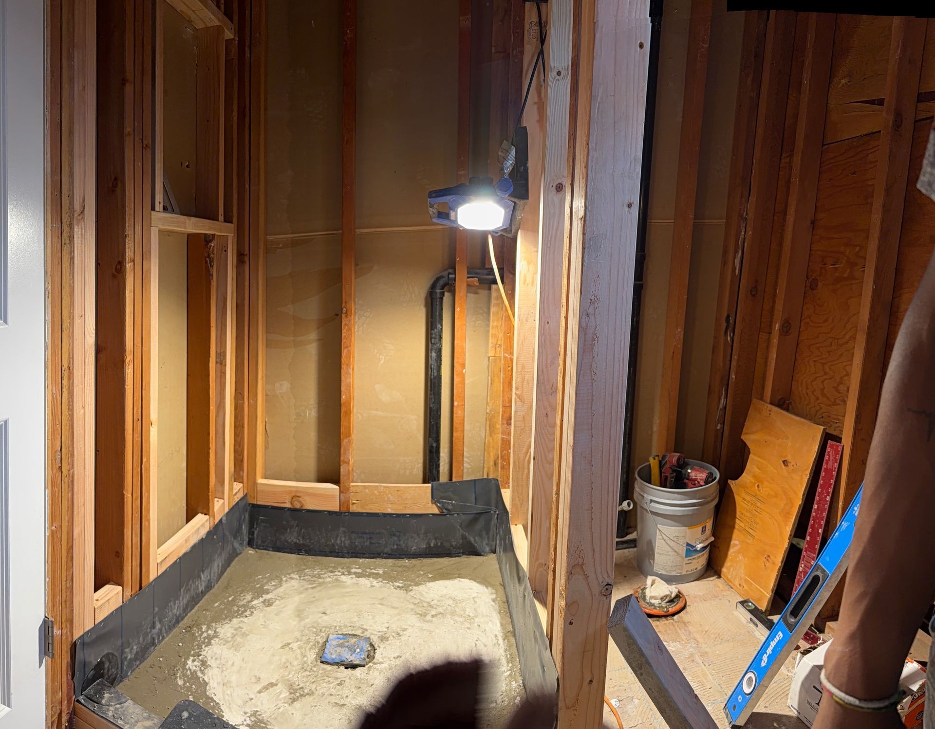 Unfinished bathroom with exposed studs, insulation, vanity light, and a bucket on the floor.