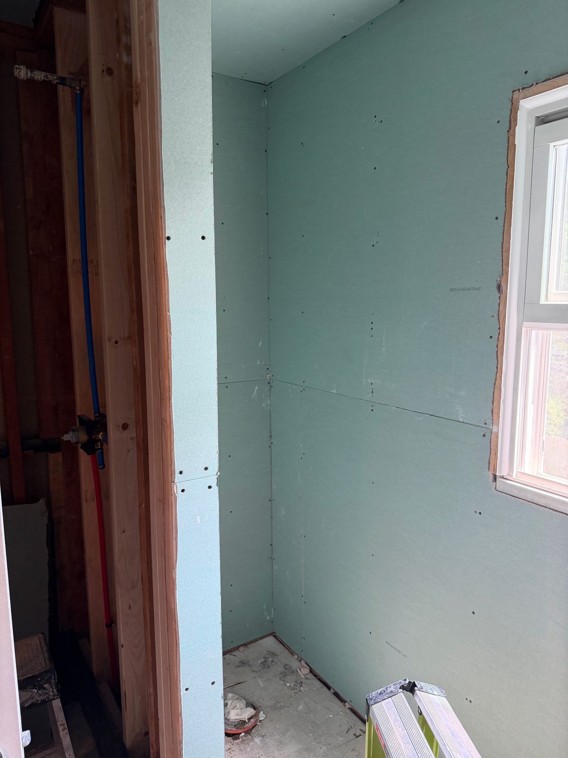 Small unfinished room with pale green walls, a window, and construction debris on the floor