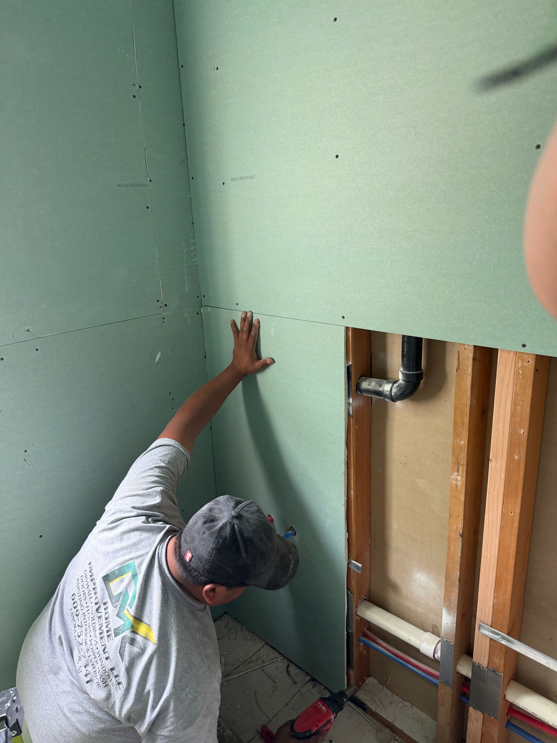Worker reaching up to mark a green wall beside exposed pipes and a doorway opening