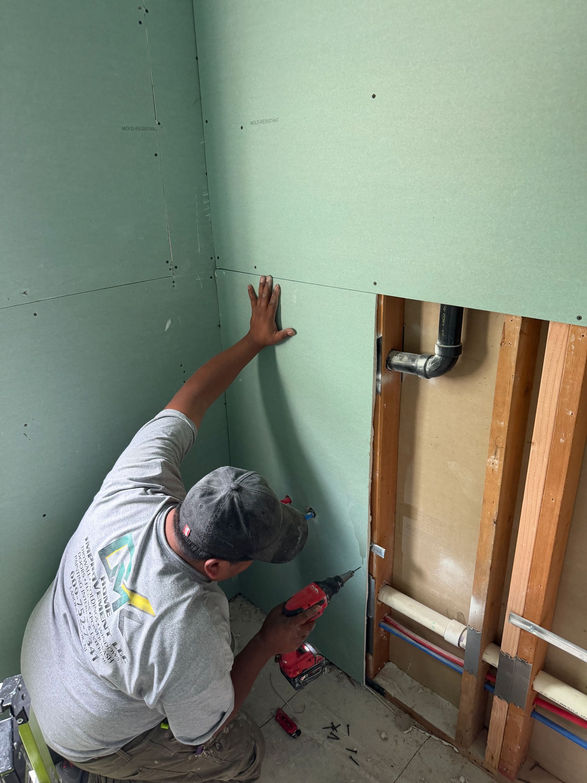 Worker painting a green wall beside exposed plumbing in an unfinished room