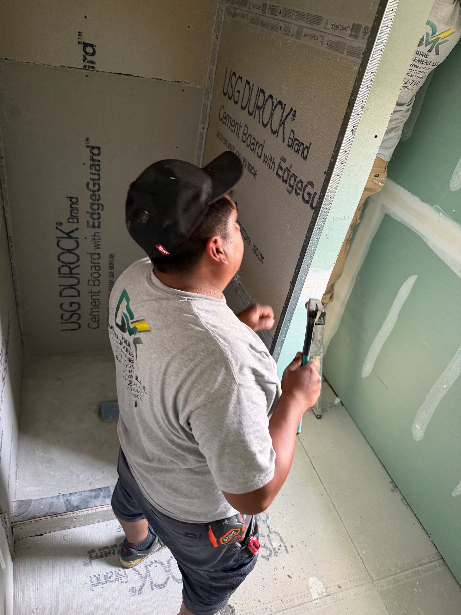 Worker installing drywall in a room under construction, seen from behind near a doorway.