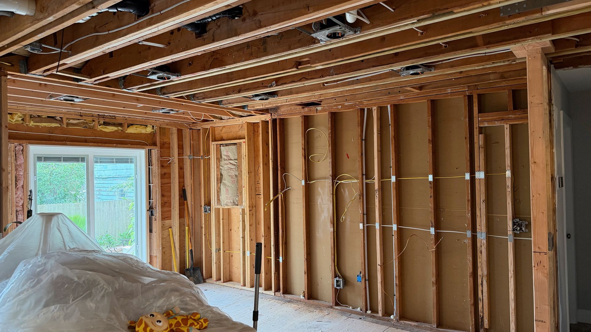 Unfinished room with exposed framing, insulation, and covered floor near a window and doorway.