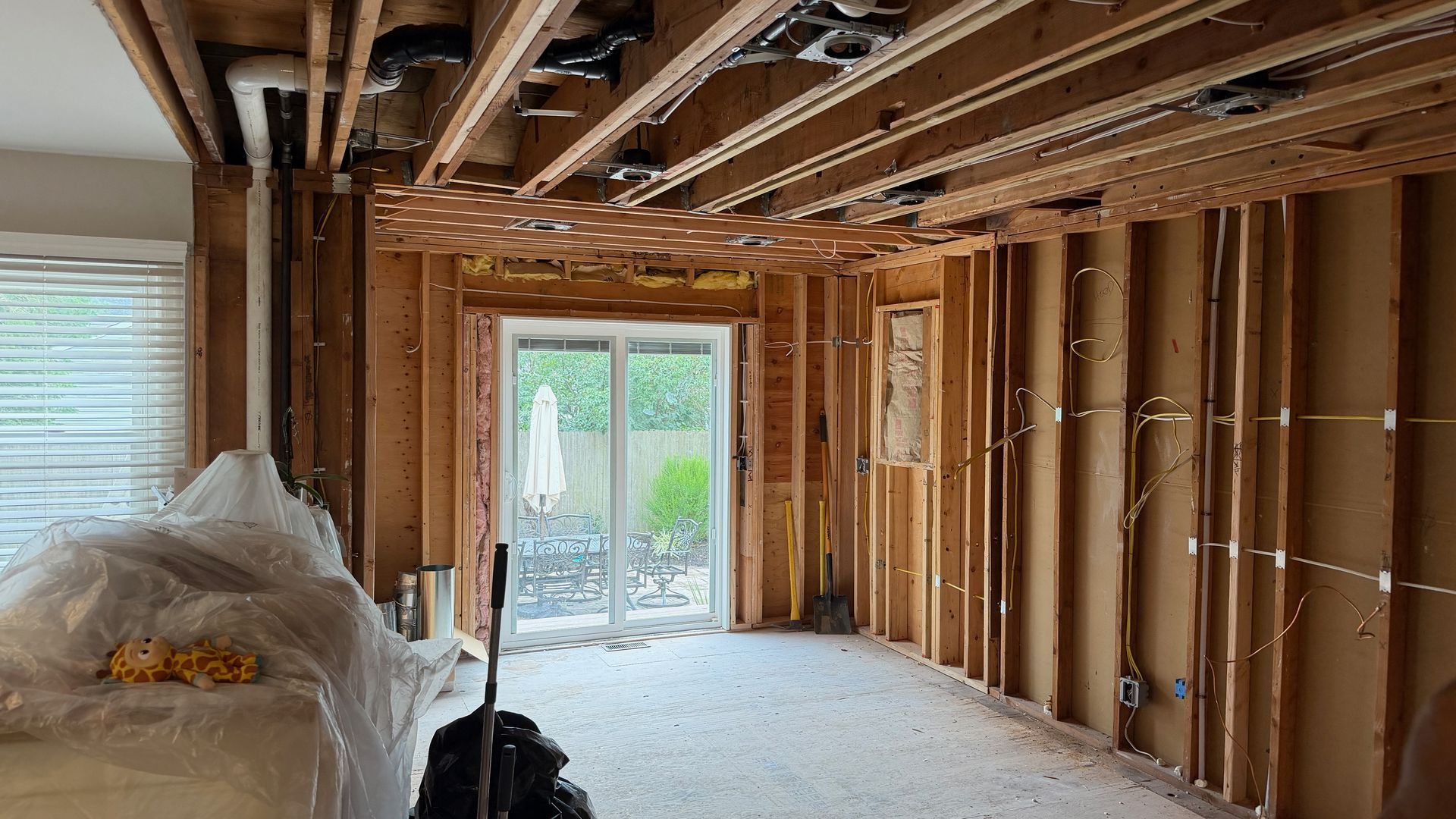 Interior under renovation with exposed ceiling joists, unfinished walls, and sliding glass doors leading outside