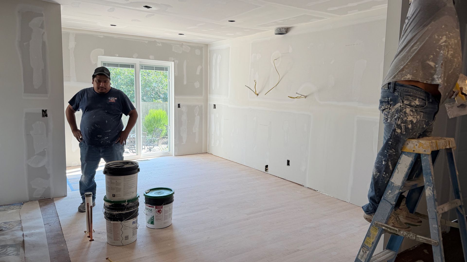 Painted room under renovation with a worker standing near buckets and a ladder by a window