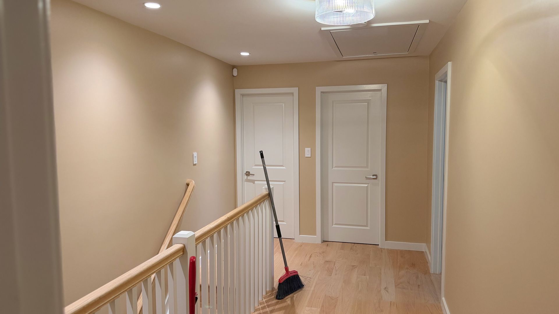 Upstairs hallway with beige walls, white railing and doors, hardwood floor, and a broom leaning near the stairs.