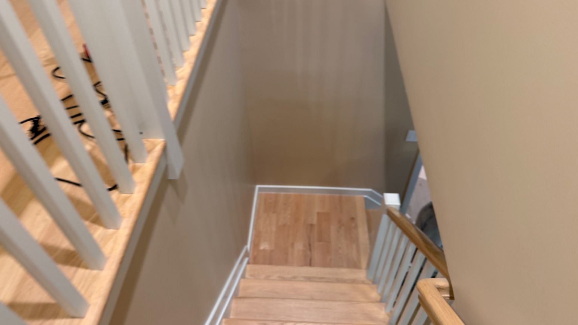 View down a narrow indoor staircase with beige walls, wooden steps, and white railing.