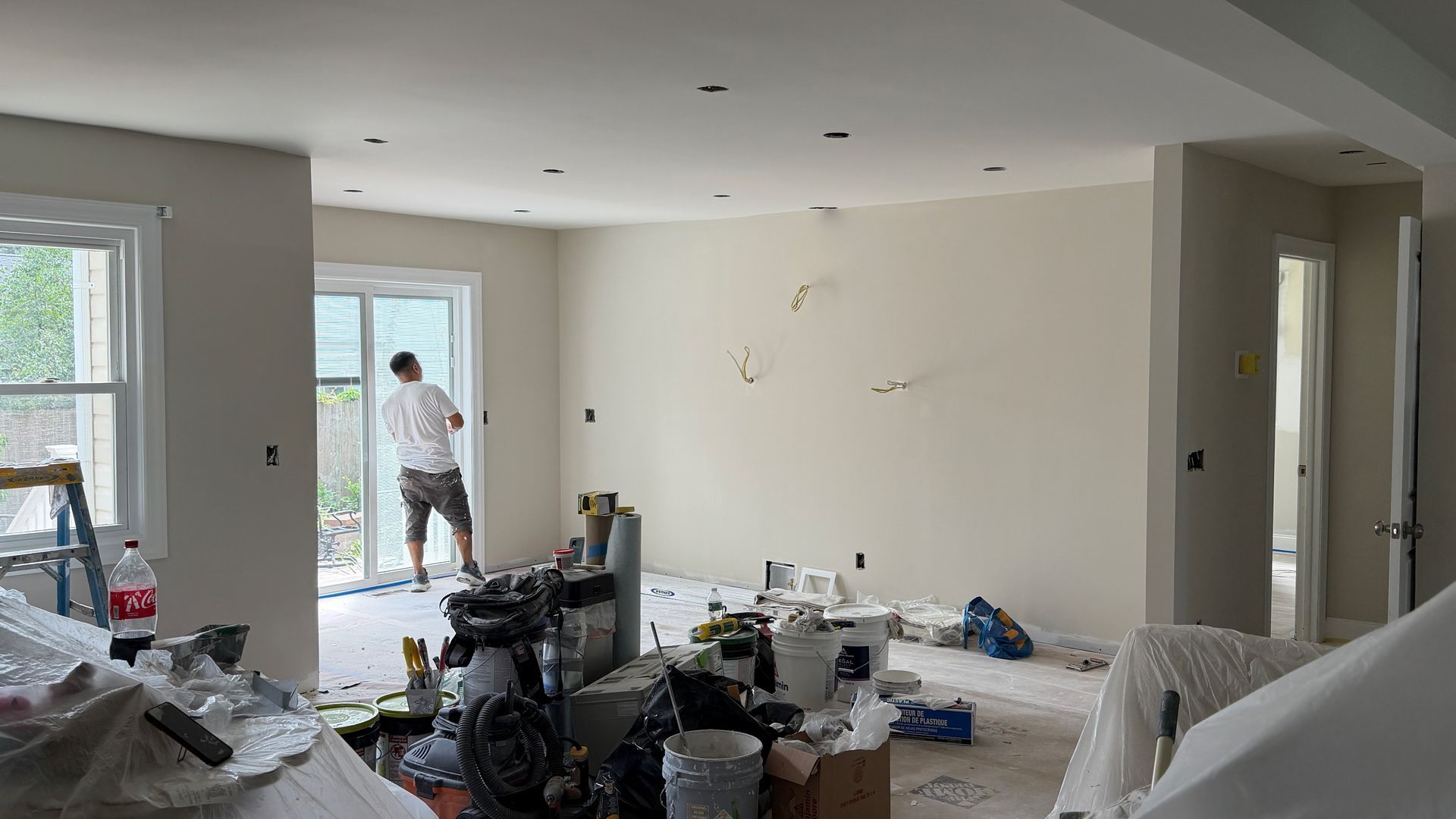 Partially renovated living room with scattered tools and debris, worker at open doorway