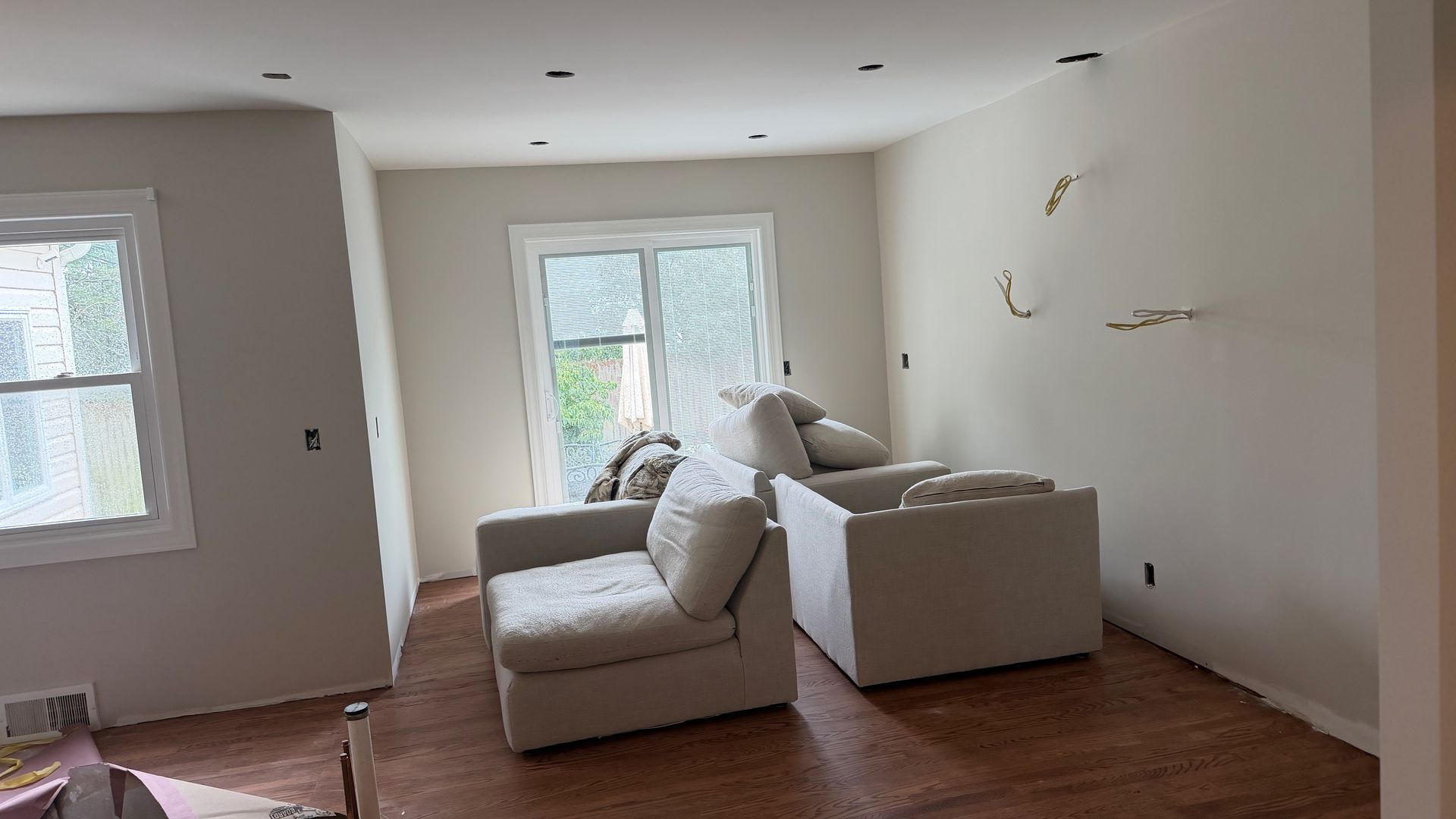 Bright living room with two beige sofas, wood floors, and a large window in the center.