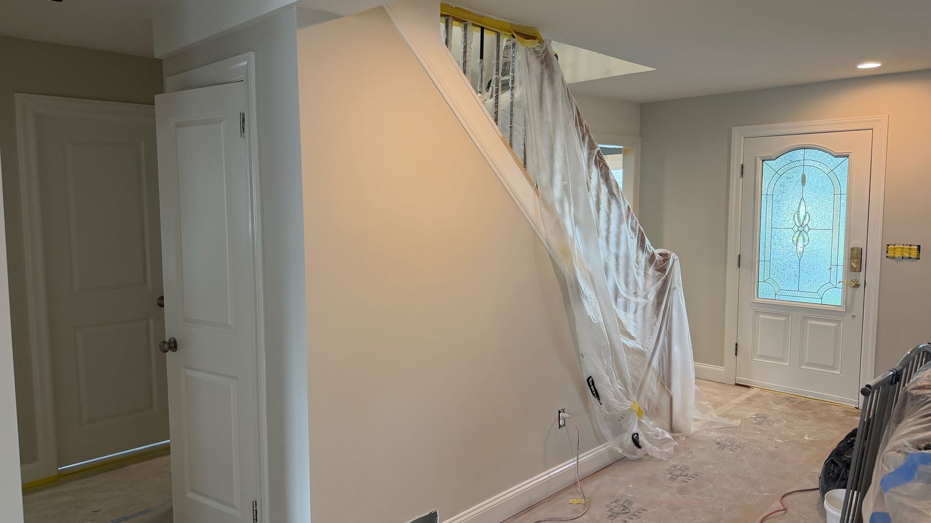 Hallway with staircase, white front door, and beige walls in a bright home interior