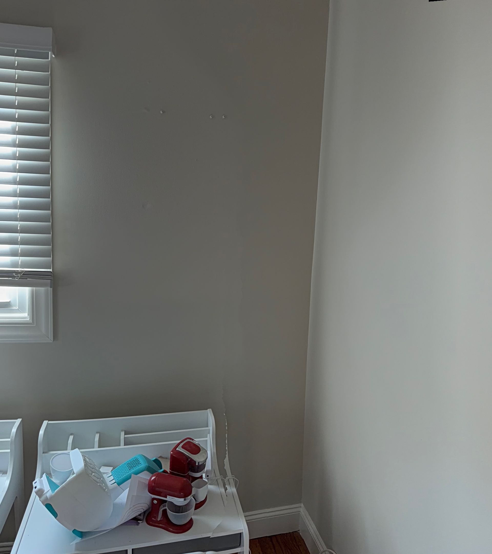 Small bedroom corner with a window, white wall, bed, and a pile of clothes and items on the floor