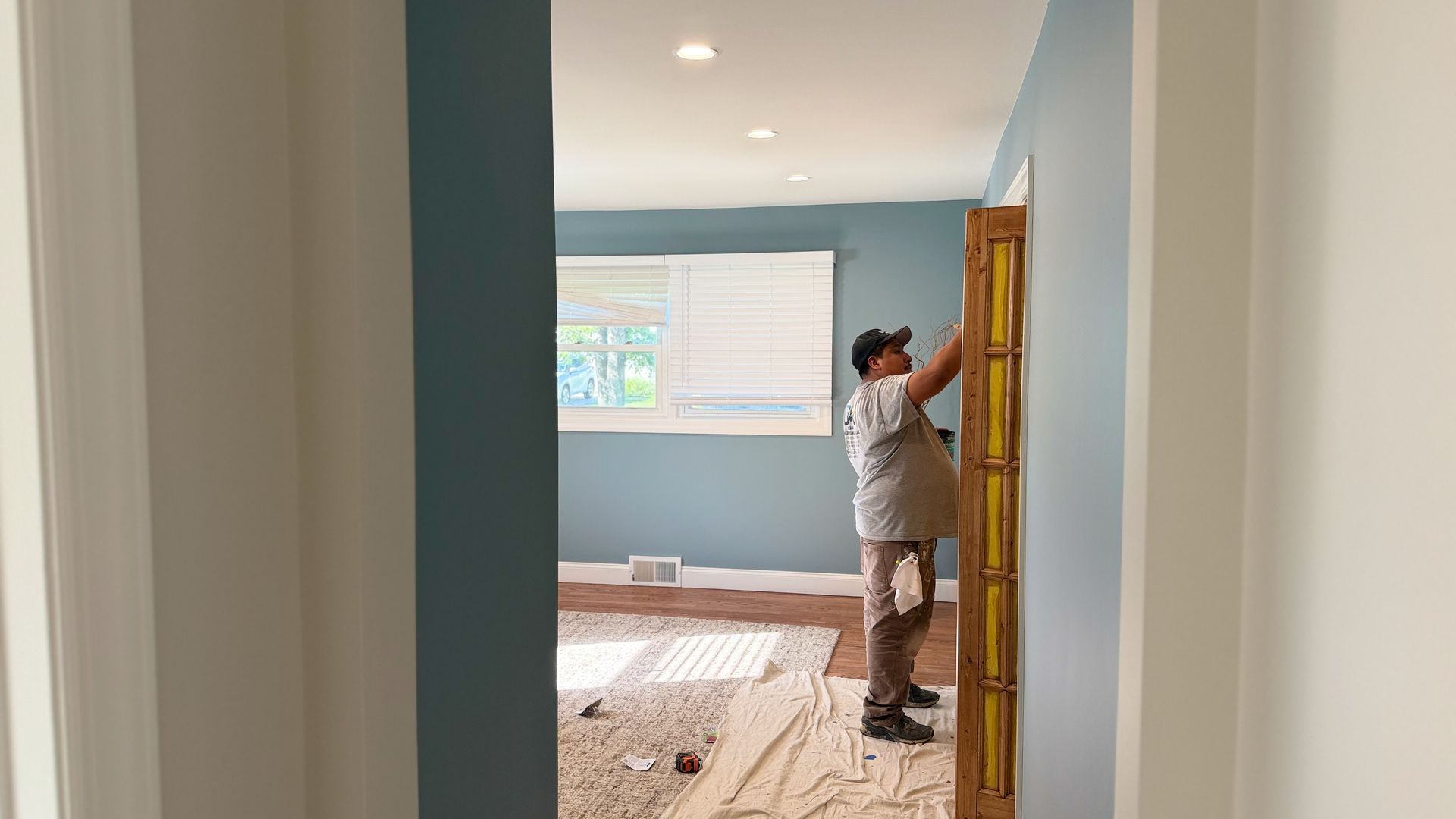 Person hanging a framed picture in a light blue room with hardwood floors