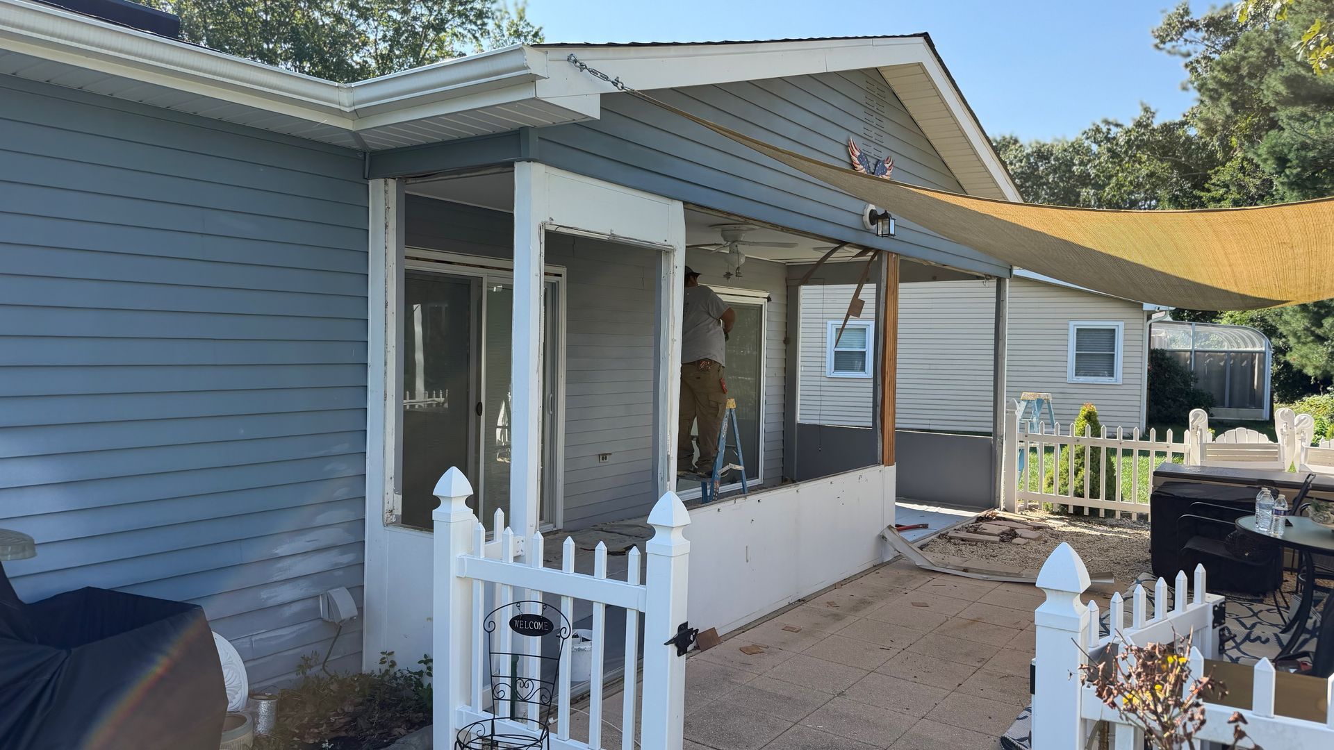 Front porch of a gray house with white trim and a small white fence in a sunny yard
