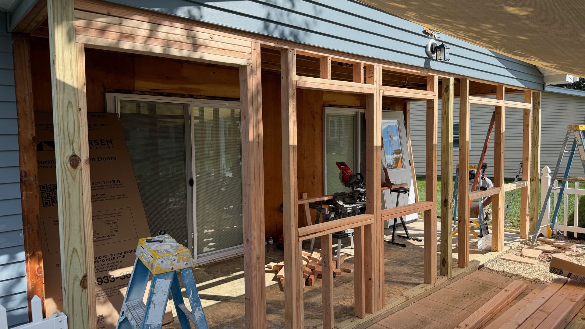 Partially framed porch addition on a house with wood studs, ladder, and construction materials