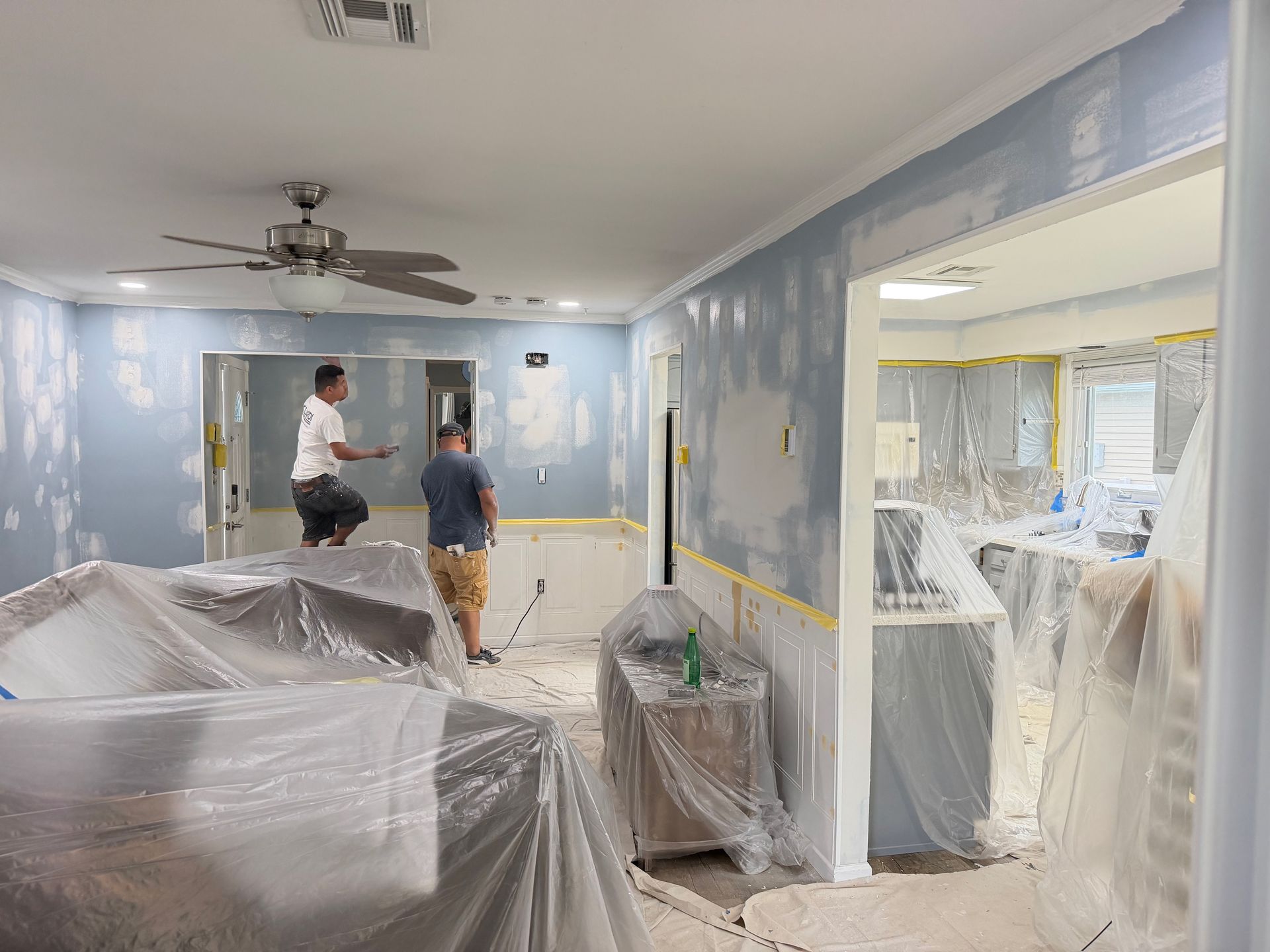 People working in a home with furniture covered in plastic during interior renovation. People working in a home with furniture covered in plastic during interior renovation.