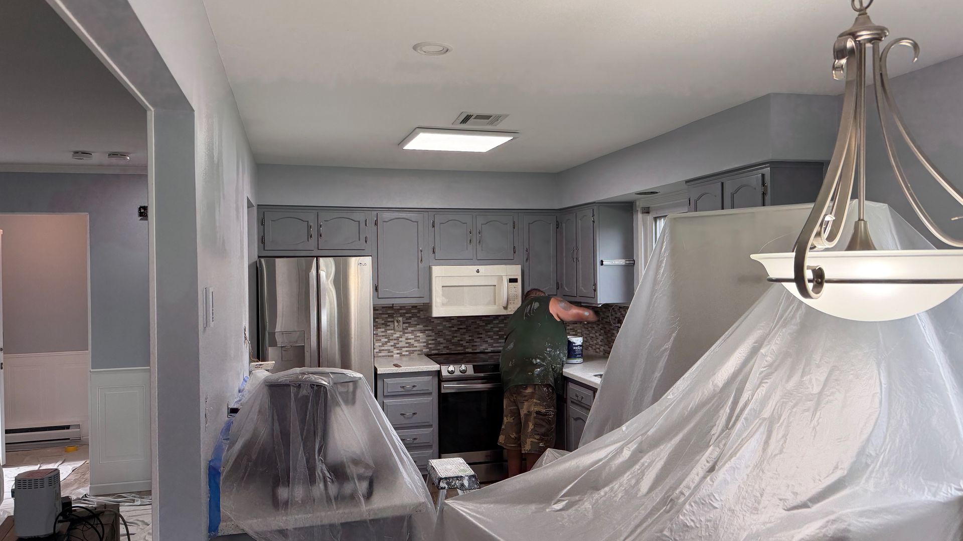 Kitchen covered in plastic sheeting during renovation, with stainless steel appliances and gray cabinets.