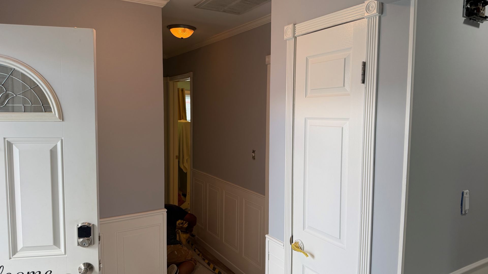 Hallway with open white doors, beige walls, and a lit ceiling fixture