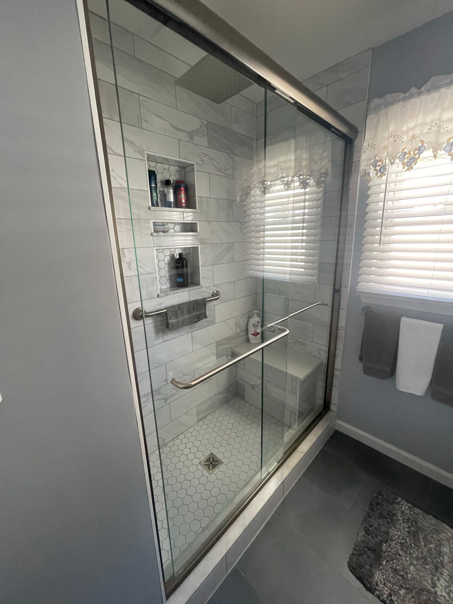 Modern bathroom shower with glass door, white tile, and wall-mounted shelves beside a window. Modern bathroom shower with glass door, white tile, and wall-mounted shelves beside a window.