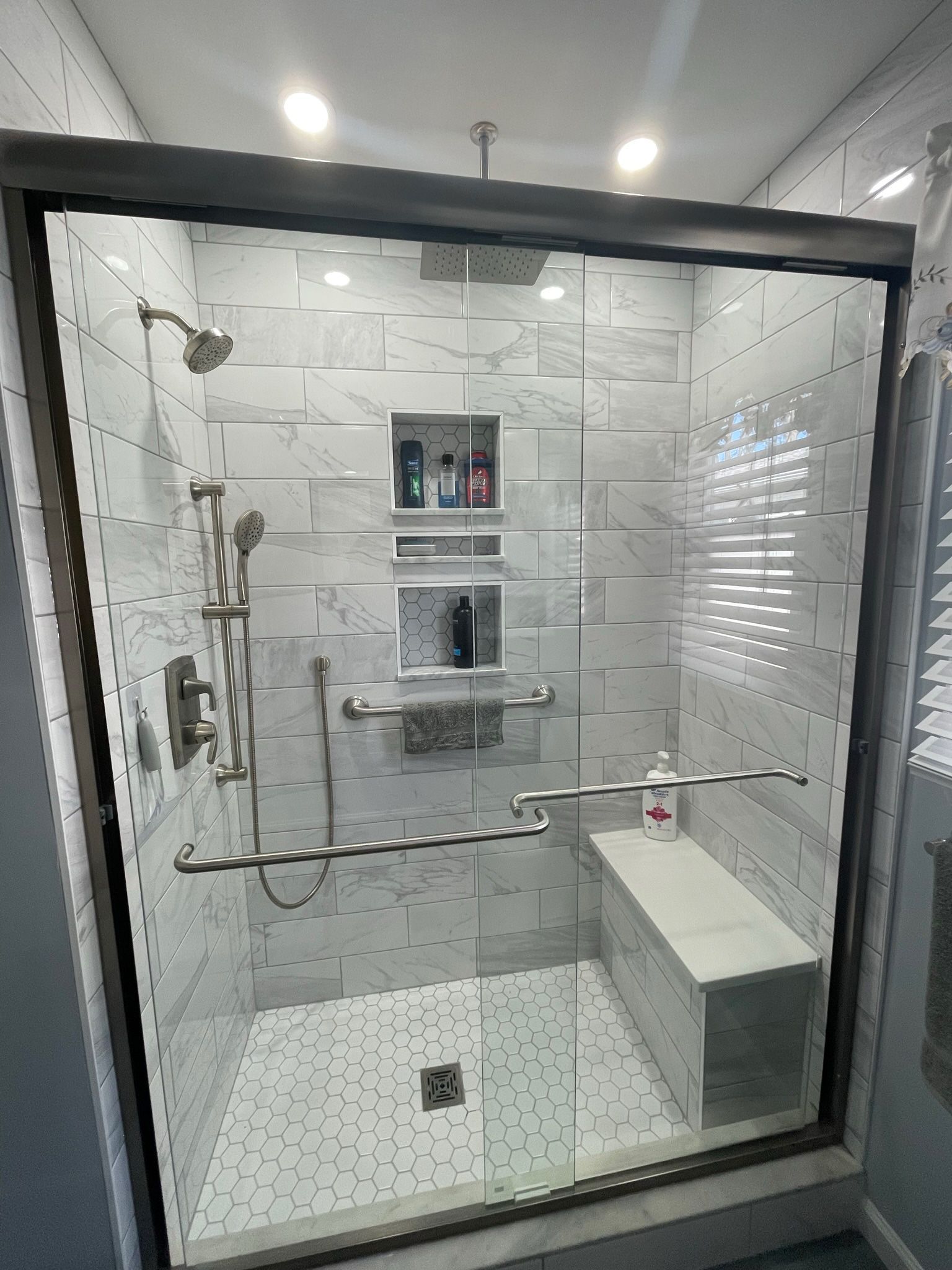 Accessible tiled shower with grab bars, built-in bench, handheld showerhead, and chrome fixtures. Accessible tiled shower with grab bars, built-in bench, handheld showerhead, and chrome fixtures.