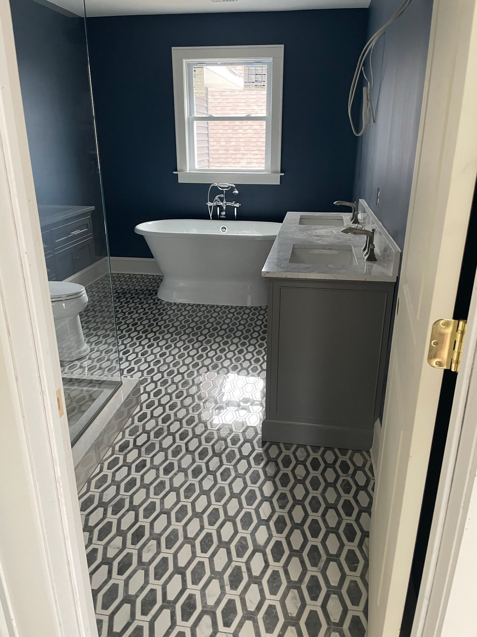 Navy bathroom with patterned tile floor, white tub, gray vanity, and window above the tub.
