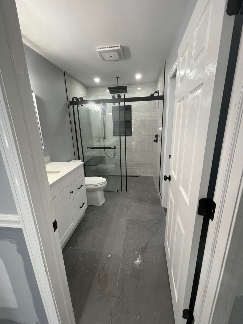 Modern bathroom with gray tile, glass shower, toilet, and vanity seen through open doors Modern bathroom with gray tile, glass shower, toilet, and vanity seen through open doors