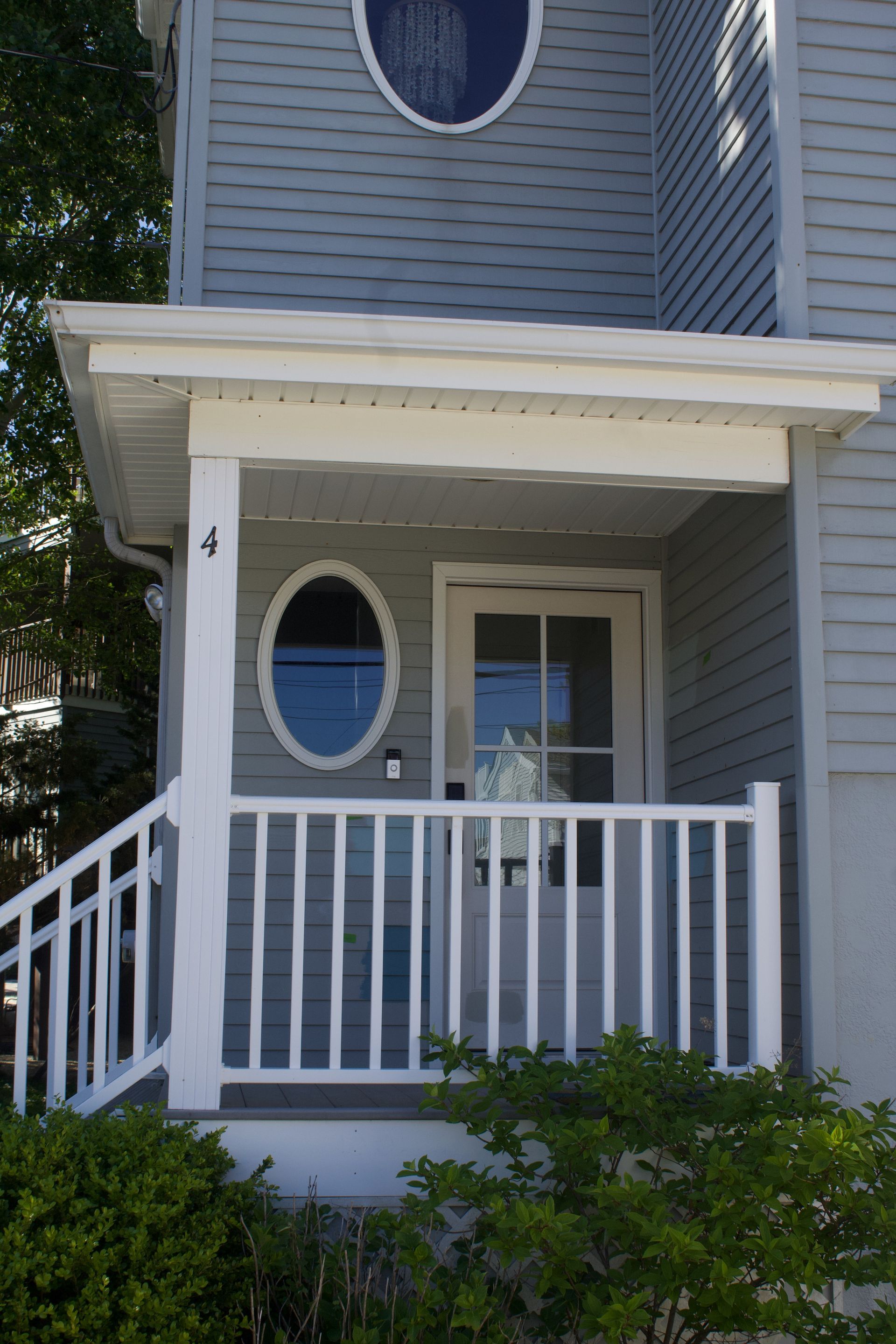 Blue house front porch with white railing and oval window at the entrance