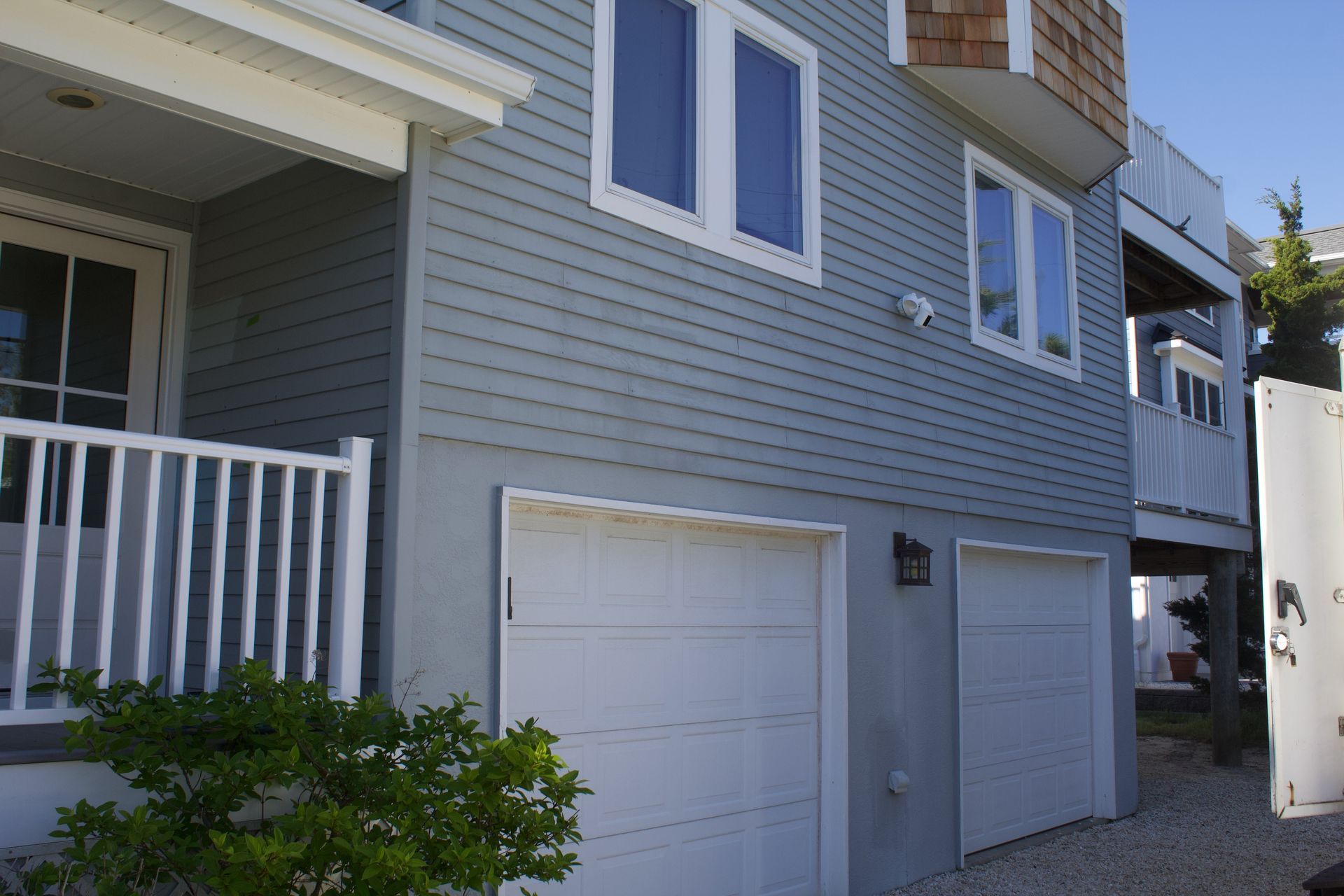 Exterior of a gray townhouse with white garage doors and a small front porch and balcony.