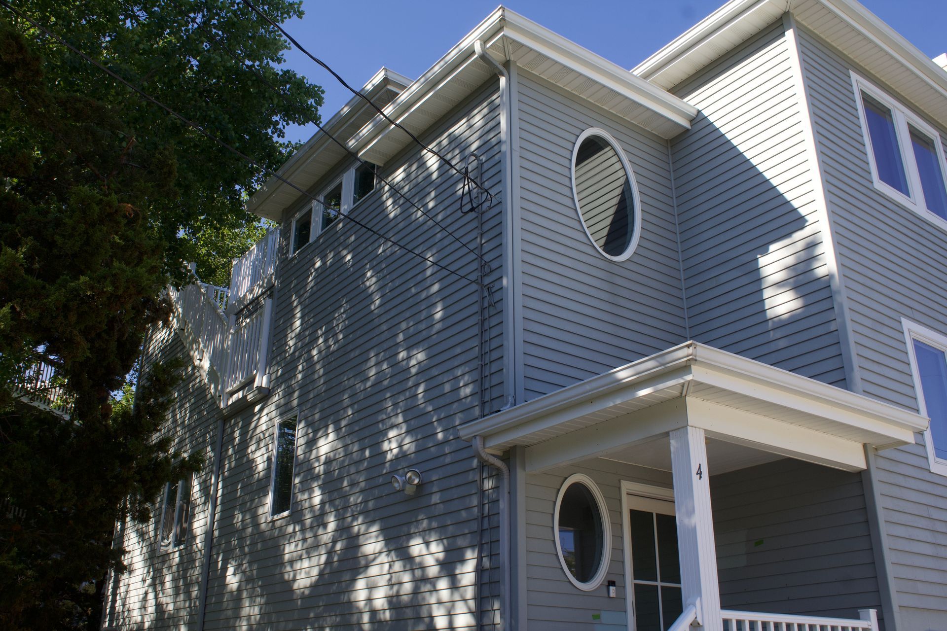 Gray two-story house exterior with white trim and round windows in sunlight