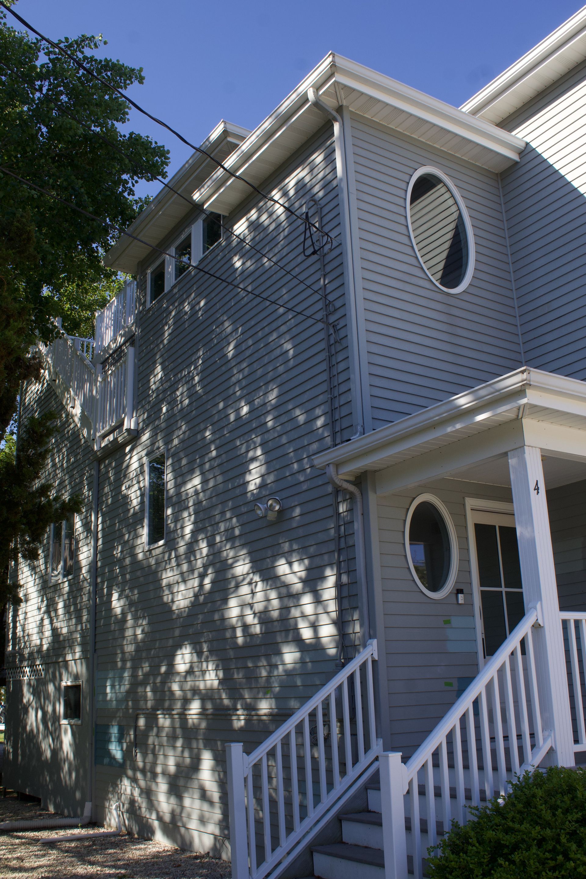 Gray house exterior with white trim, front porch, and round windows in sunlight