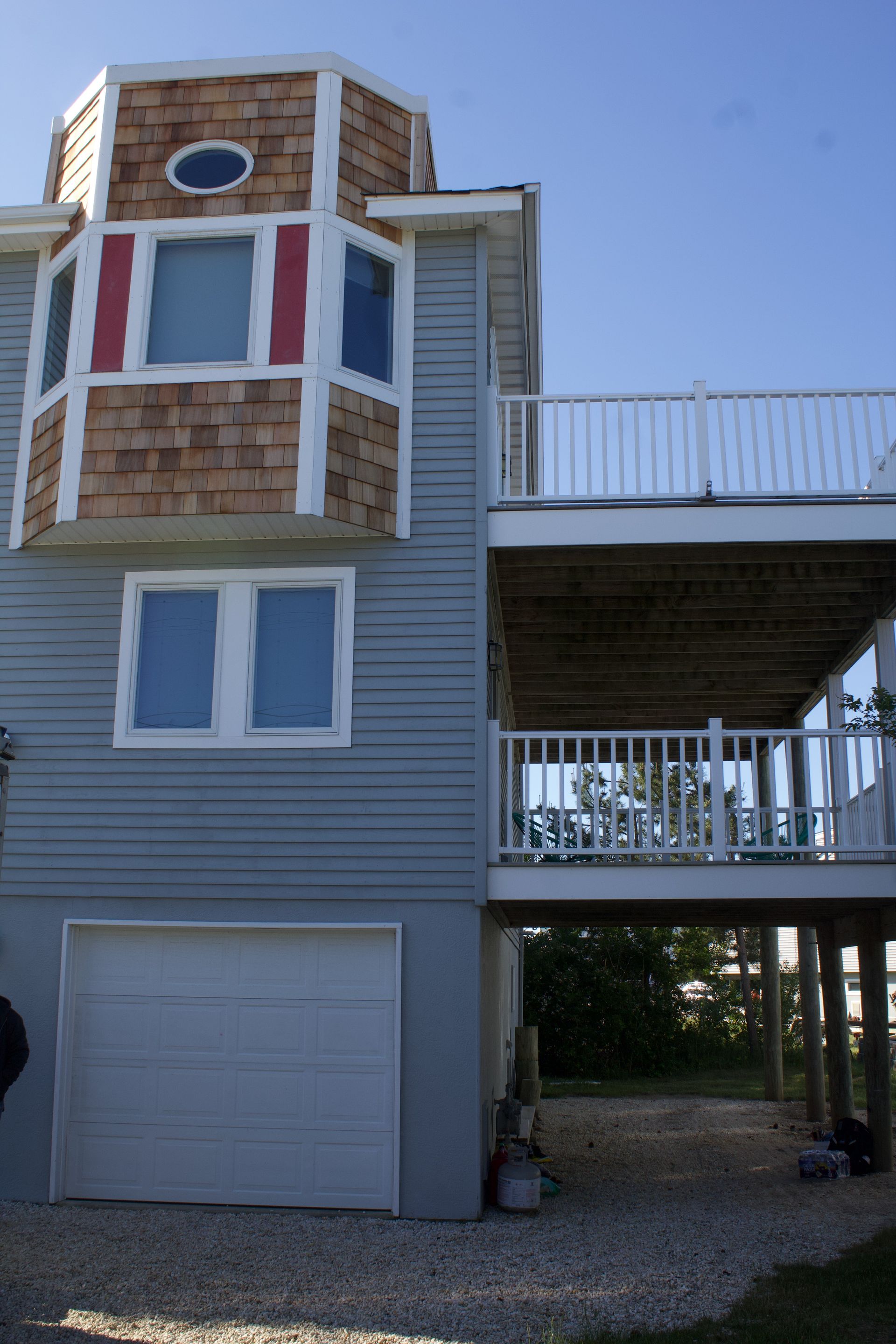 Three-story beach house with gray siding, red bay windows, and an attached deck over a garage.