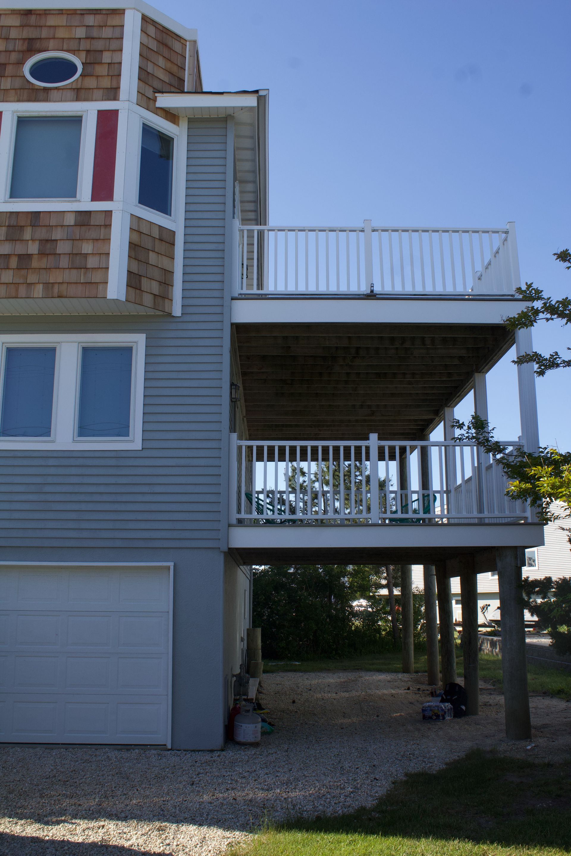 Two-story gray house with a large raised deck and a garage below, viewed from the side