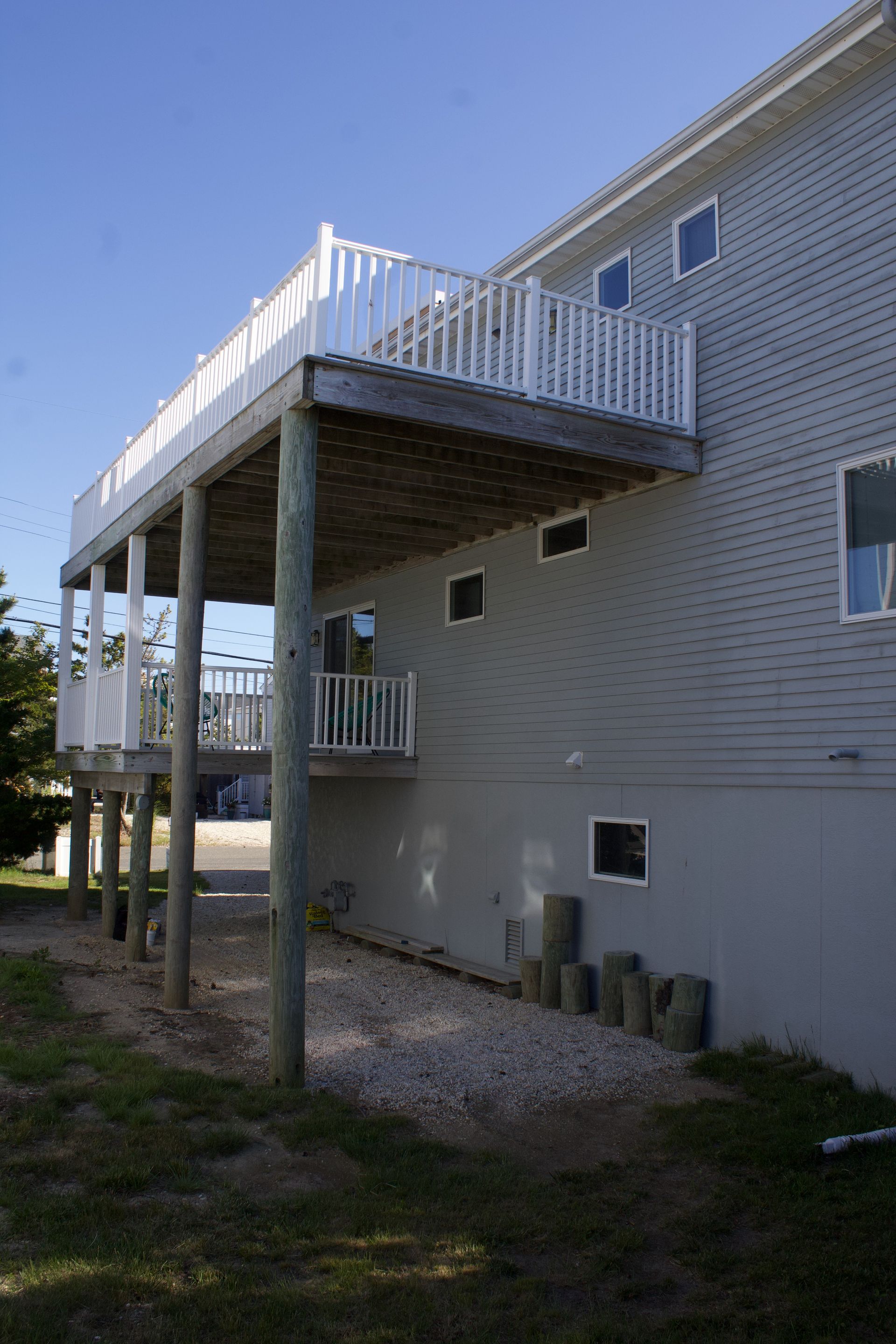 Raised wooden deck attached to a white brick house, with stairs and railing on the side.