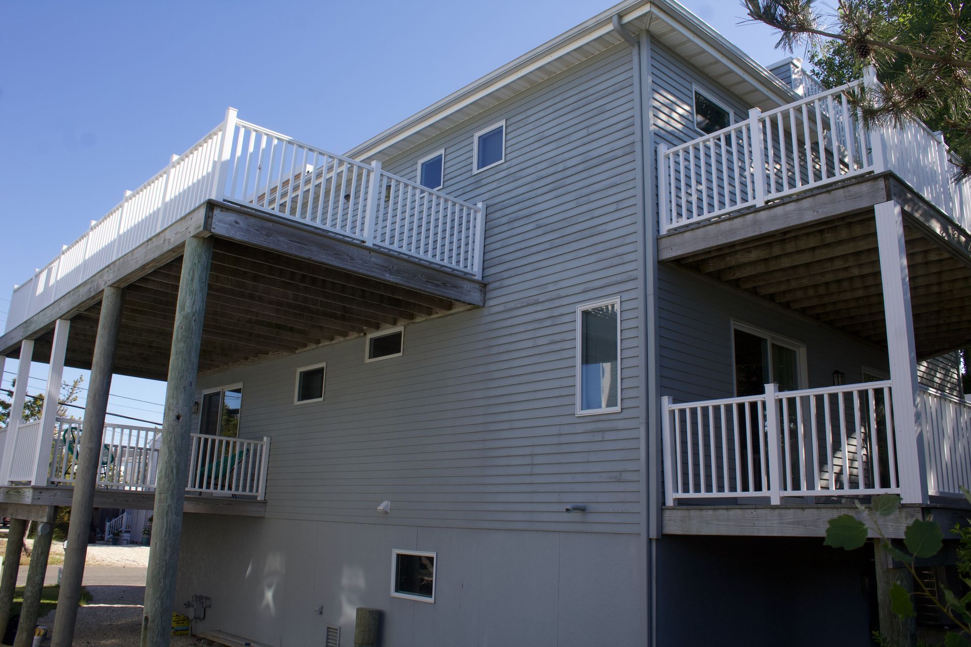 Two-story gray house with white railings and raised decks on a sunny day