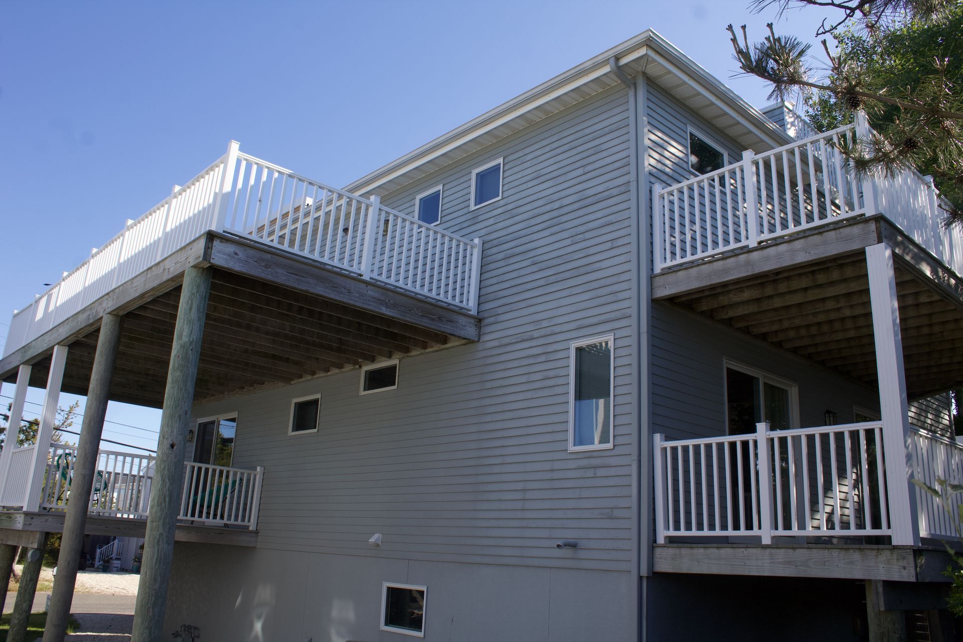 Gray two-story house with white railings and decks on a sunny day