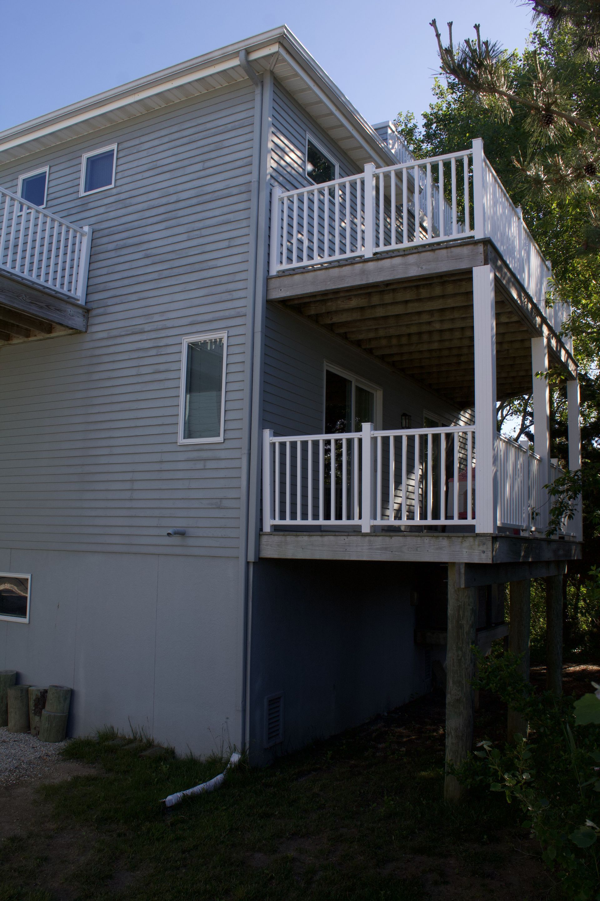 Two-story gray house with white railings and stacked balconies on a grassy lot