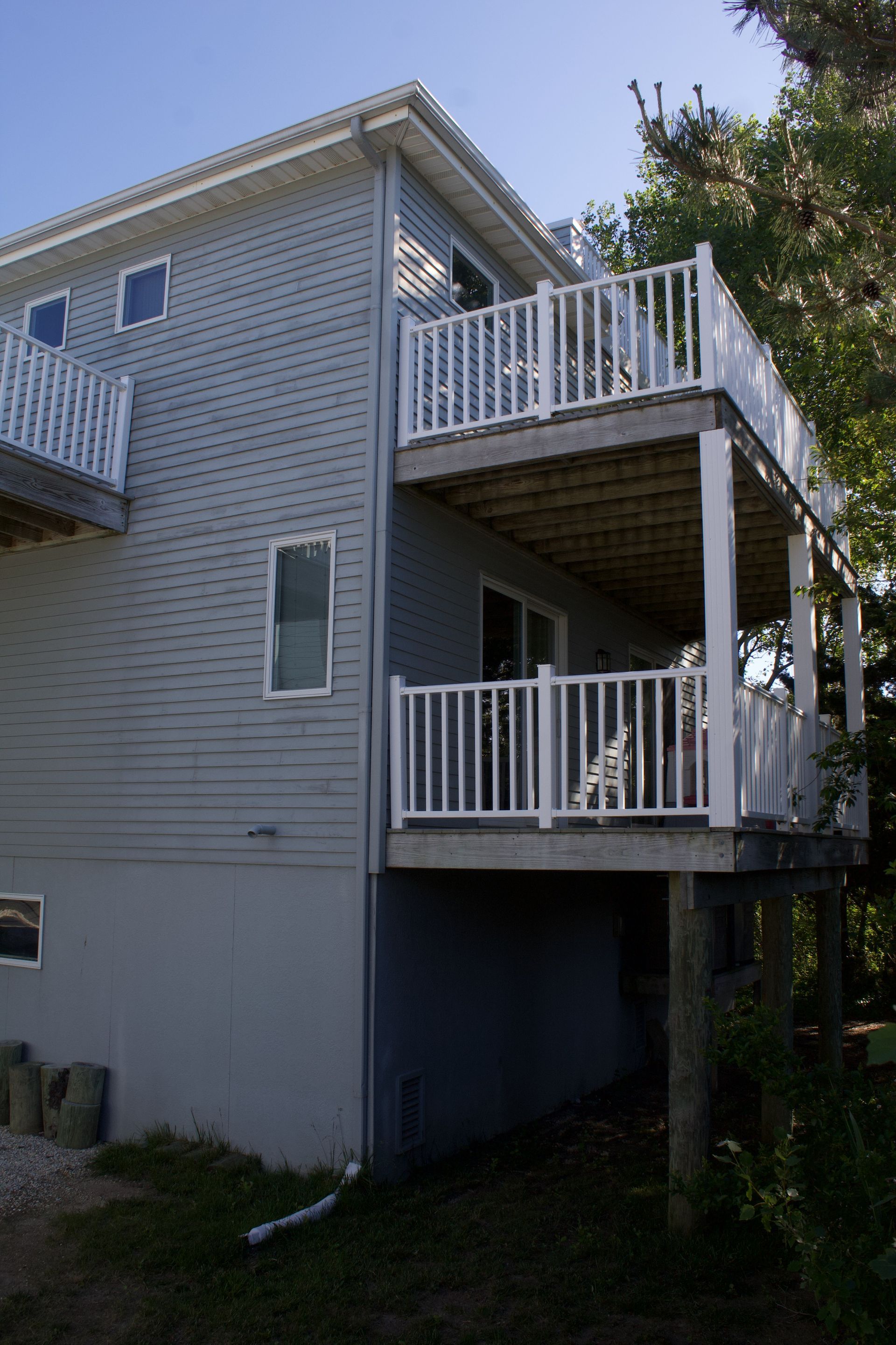 Side view of a gray house with two white-railed balconies and a grassy yard.