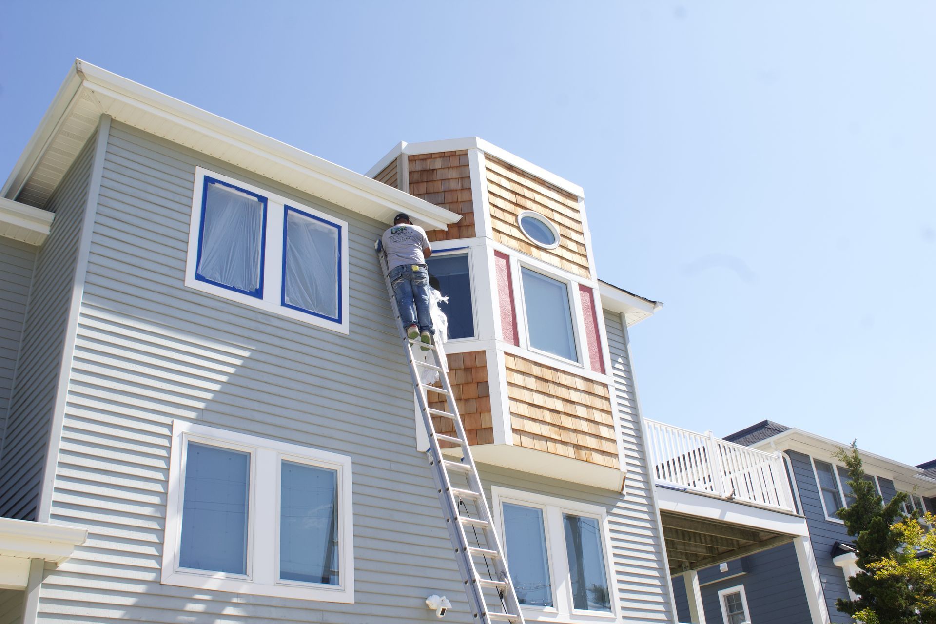 Worker on a ladder repairing the exterior of a beige townhouse under a clear blue sky